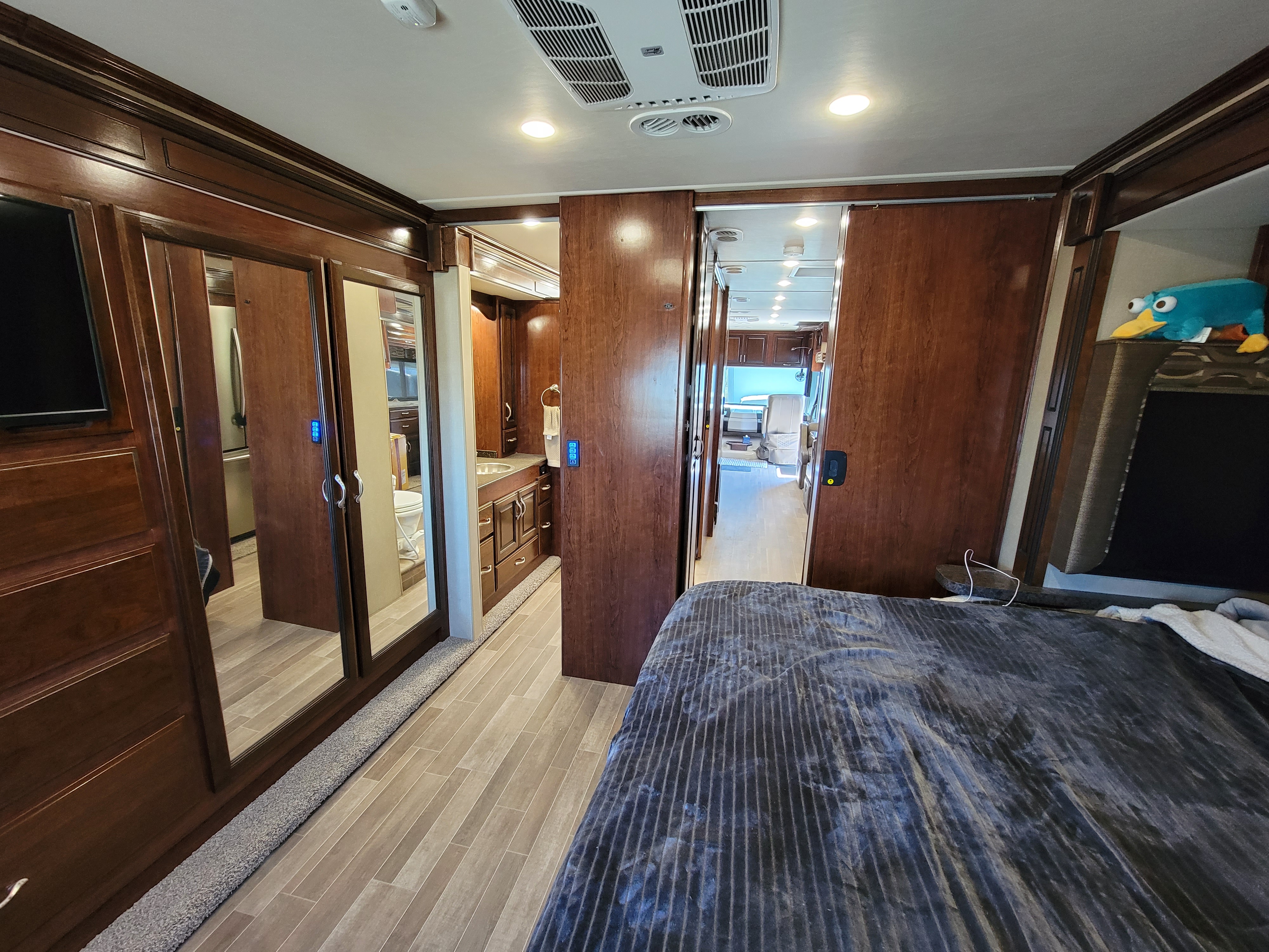 RV rental interior: bedroom with dark wood & mirrored closets, leading to bathroom & living space. Plush toy adds a homey touch.. Fleetwood Other 2018