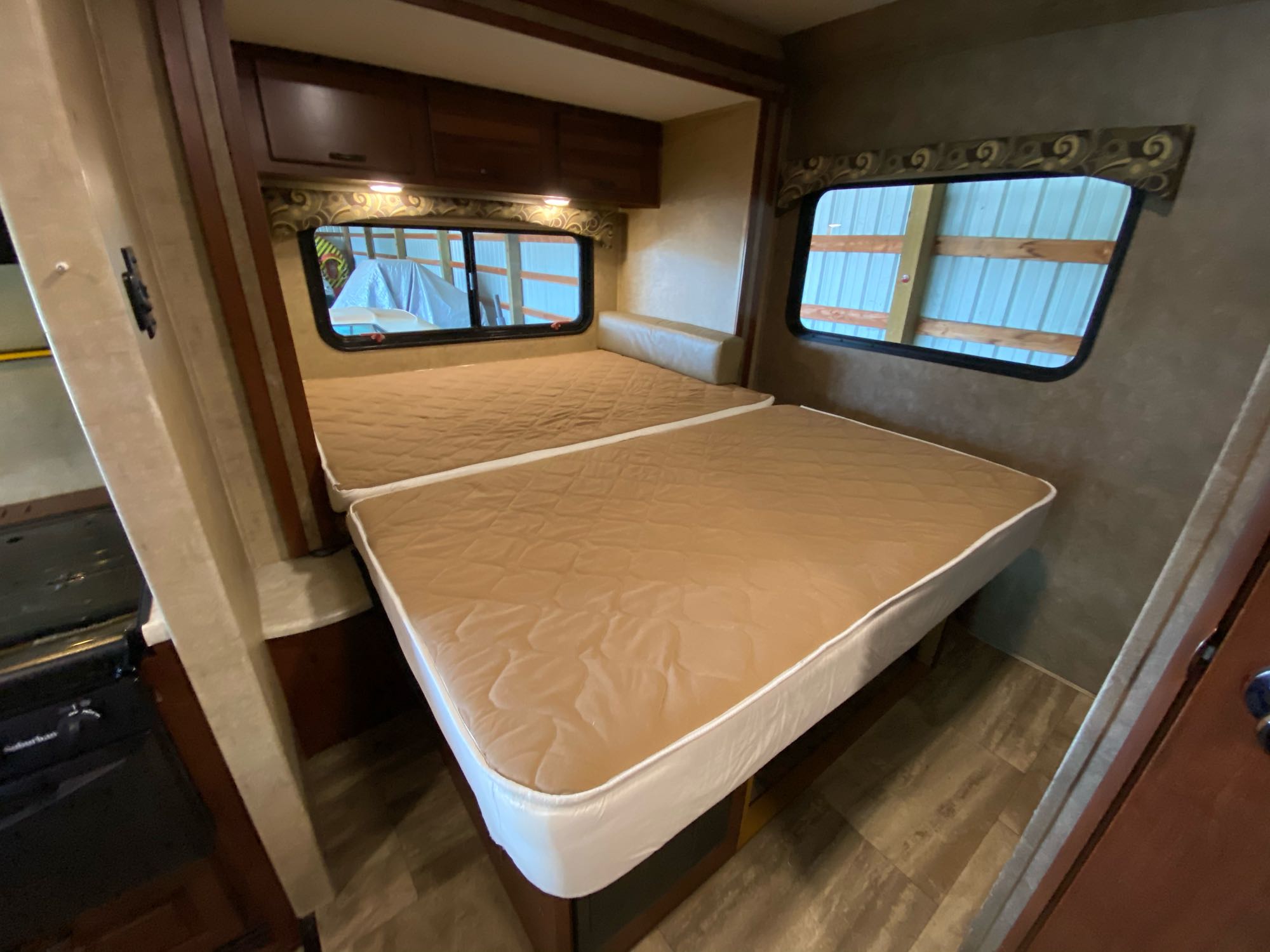 Inside an RV rental: View of two comfortable beds with quilted covers, overhead storage, and large windows in the sleeping area.. Forest River 2700DS 2016