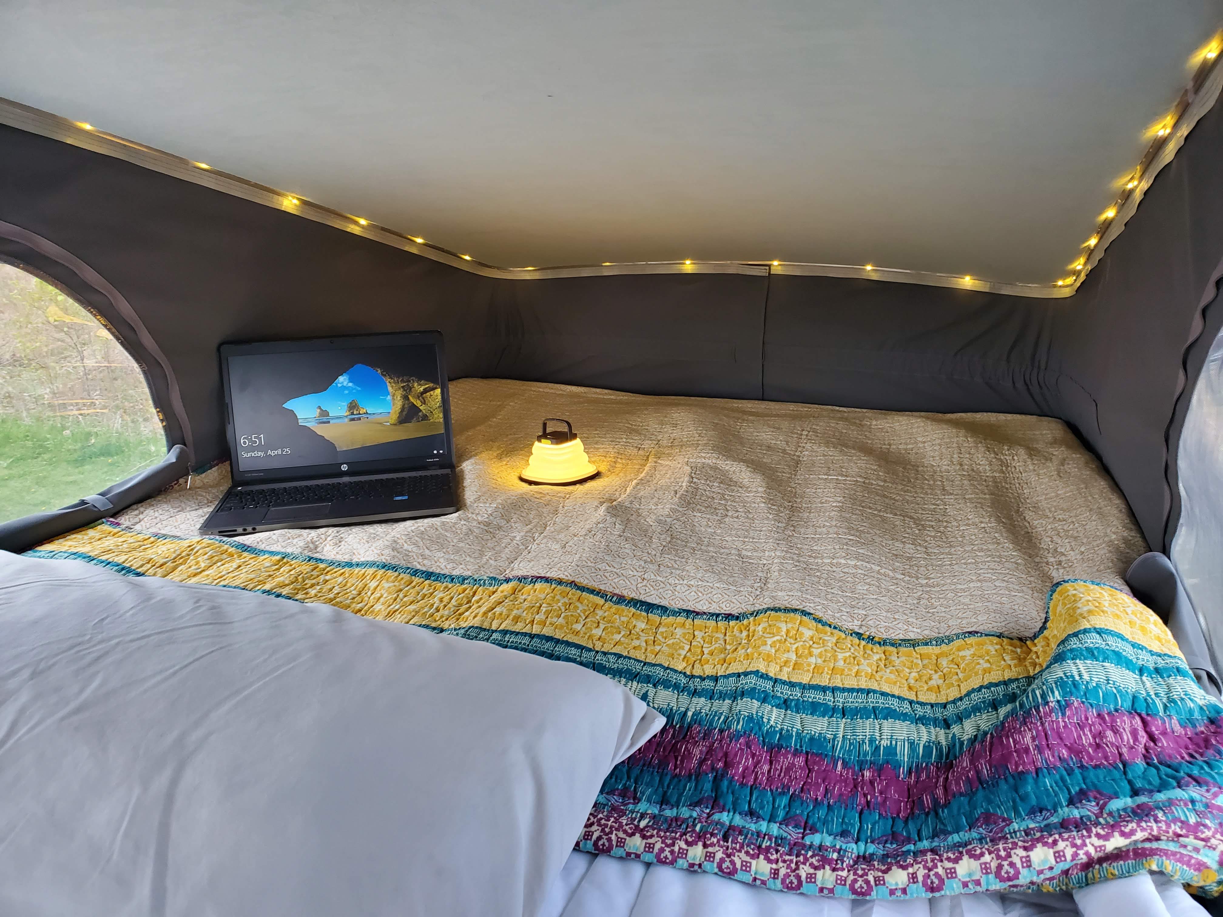 Cozy RV rental bed setup: laptop, glowing lantern, and warm string lights create a perfect mobile workspace.. Winnebago Solis 2022