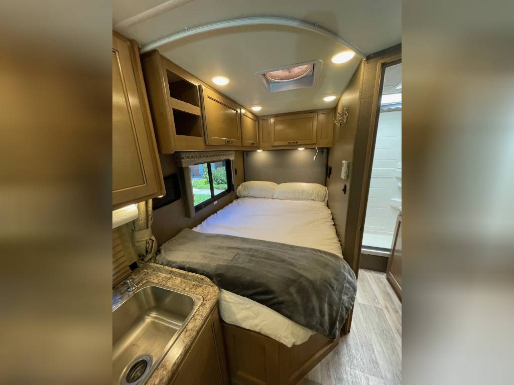 RV rental interior: cozy bed, compact kitchen with sink, and private bathroom access visible.. Thor Motor Coach Four Winds 2019