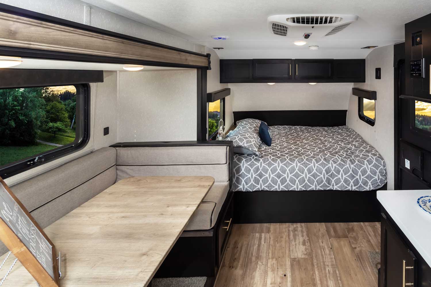 RV rental's cozy bedroom with patterned bedding and dinette seating with table, brightened by windows showing nature.. Forest River Wolf Pup 2021