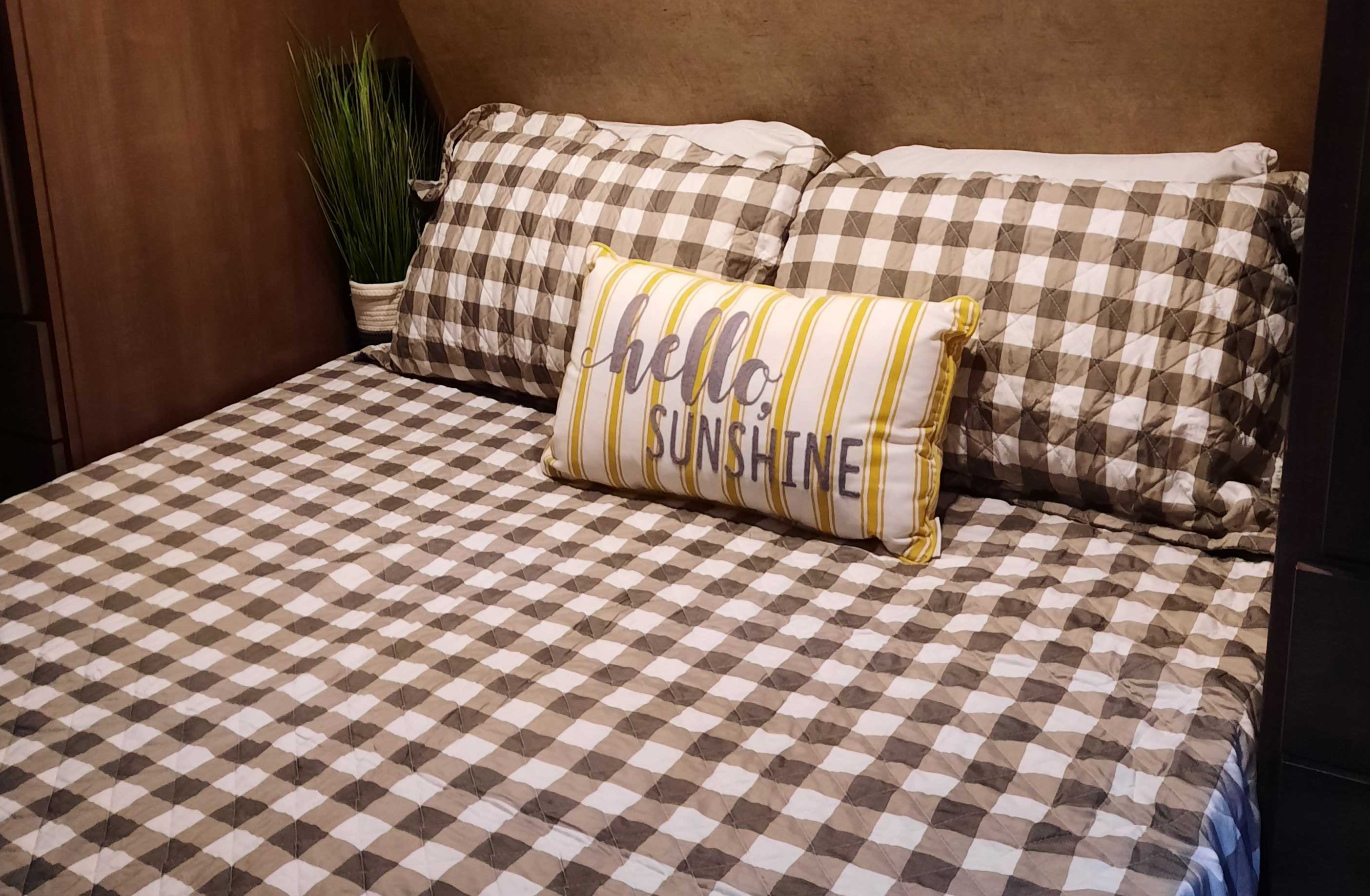 Inviting RV rental bedroom with cozy brown and white gingham bedding and a "Hello Sunshine" decorative pillow.. Forest River Surveyor 2016