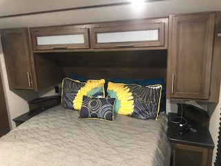 Comfortable RV rental bedroom featuring a made bed, decorative pillows, and ample overhead storage for travel.. Keystone RV Cougar 2020