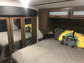 Inside this RV rental: a compact bedroom featuring a comfortable bed with vibrant pillows, overhead storage, and mirrored closet doors.. Keystone RV Cougar 2020