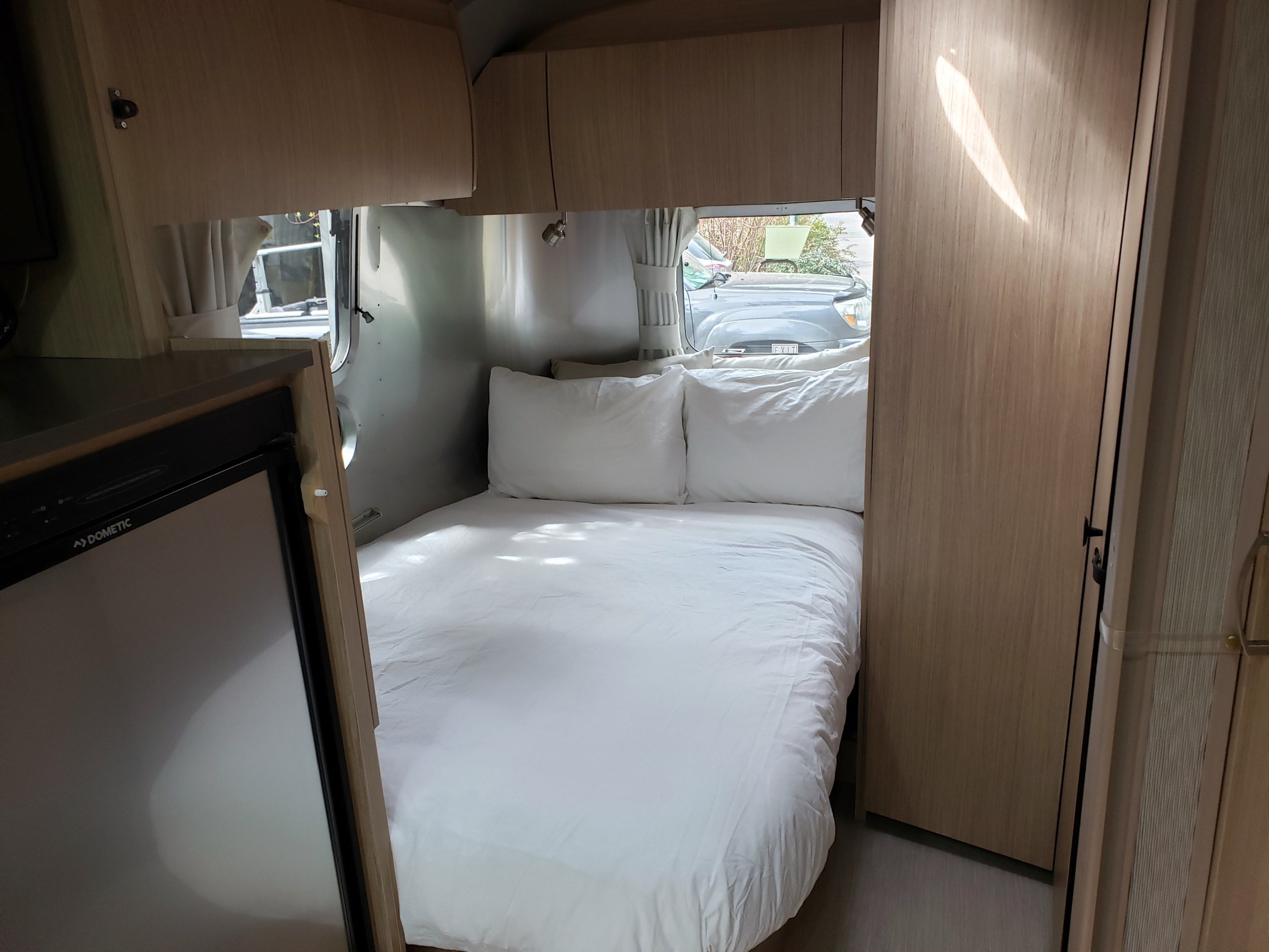 Inside a modern rv rental: white bedding, wood cabinets, and Dometic fridge. Ready for your road trip!. Airstream Flying Cloud 2018
