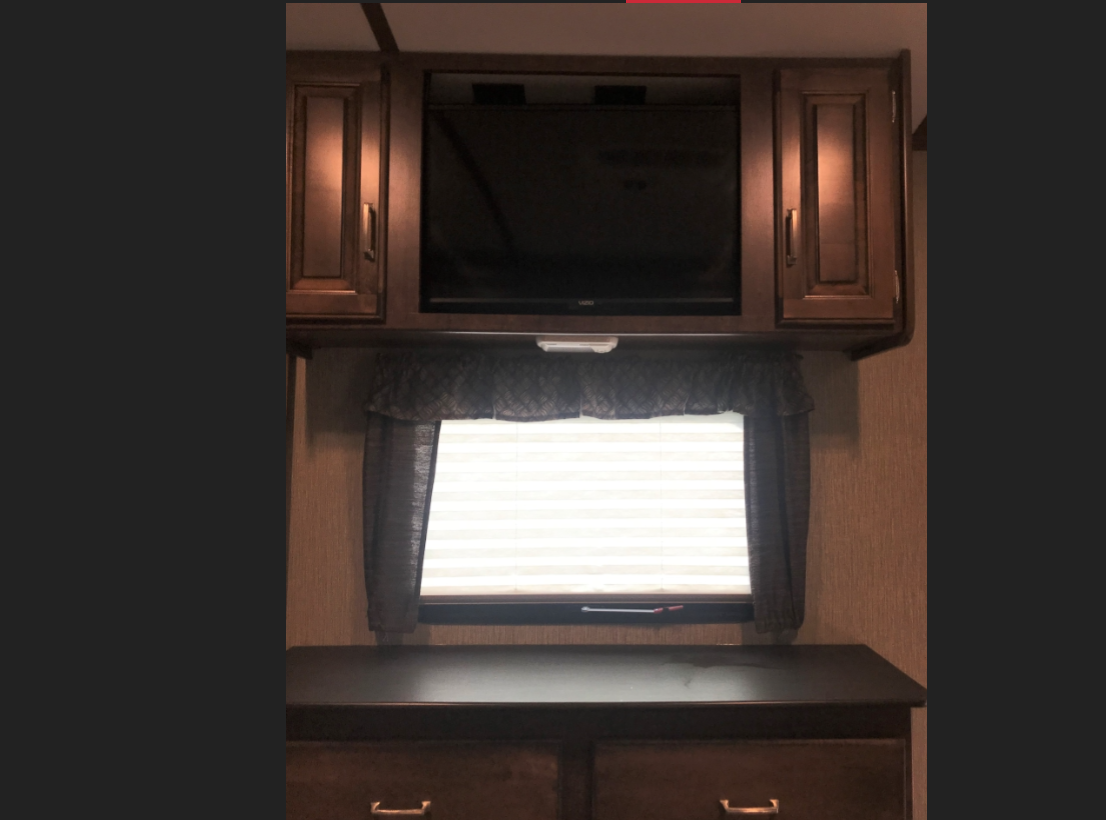 View inside an RV rental showing a TV, window with blinds, and lower dresser unit.. Keystone Outback 2018
