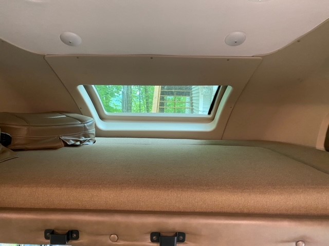 Inside an RV rental: a cozy cab-over bunk bed with a large window view of lush trees, ready for your adventure.. Tiffin Motorhomes Wayfarer 2019