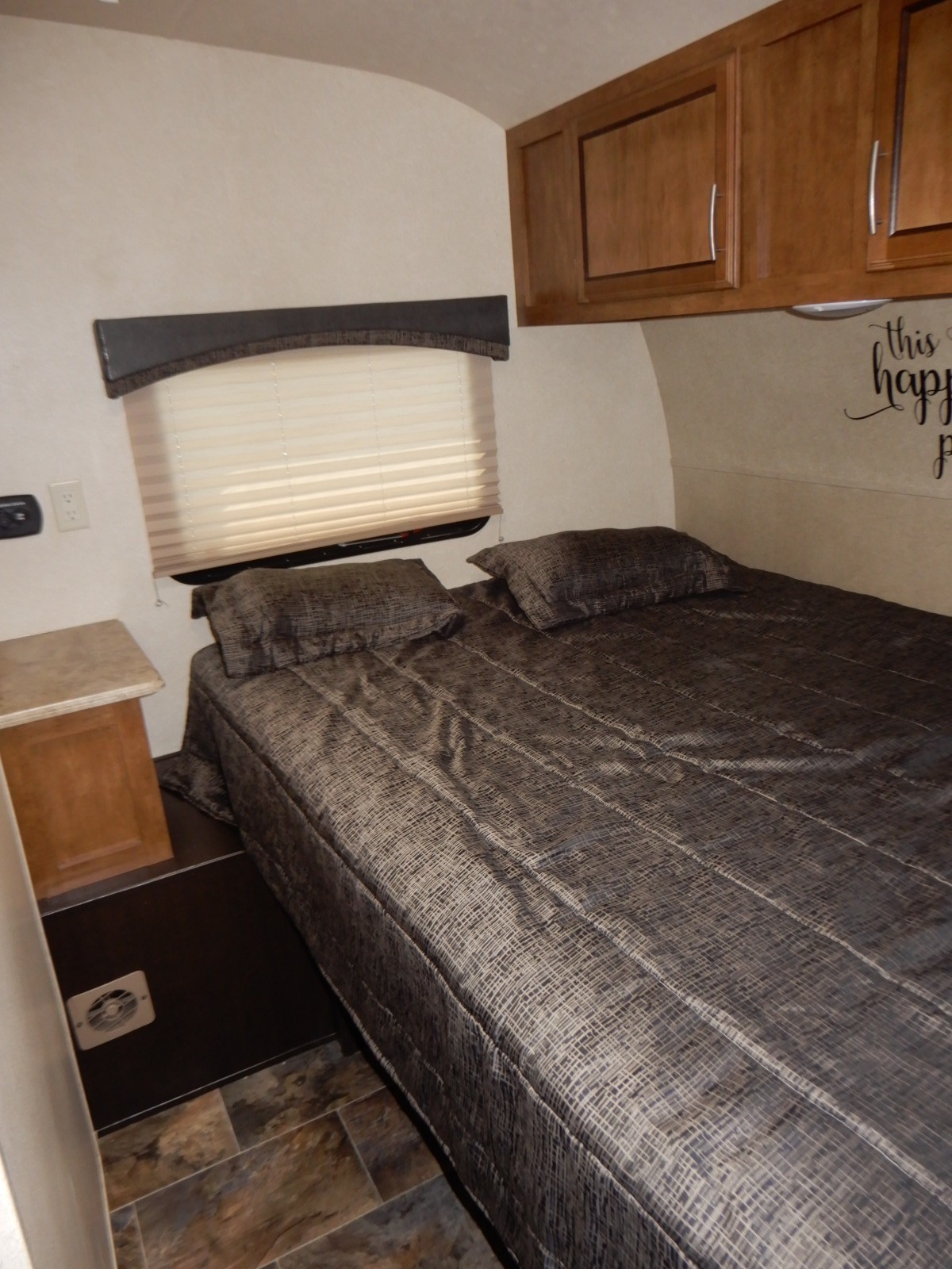 RV rental bedroom with a comfortable bed, patterned linens, wooden overhead cabinets, and a window with blinds.. Forest River Shockwave 2017