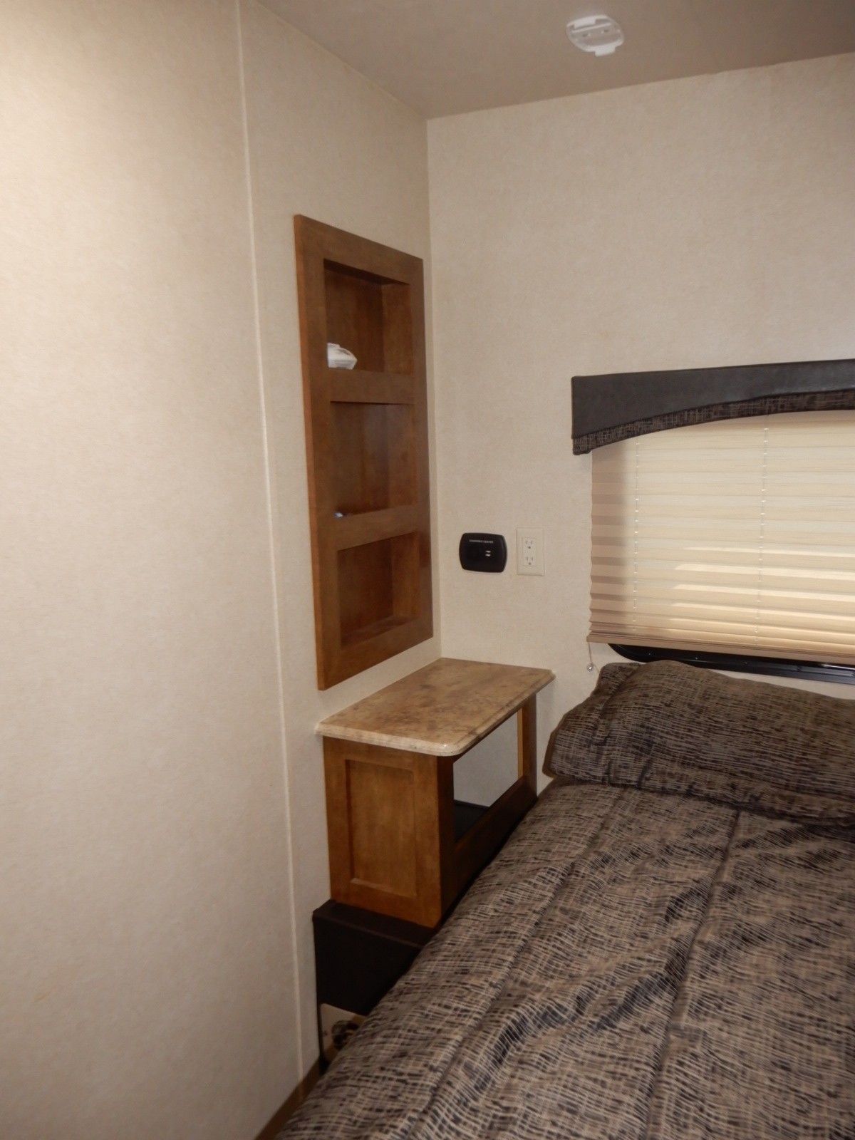 Comfortable RV rental bedroom featuring a built-in nightstand, shelves, and window with blinds for a cozy stay.. Forest River Shockwave 2017