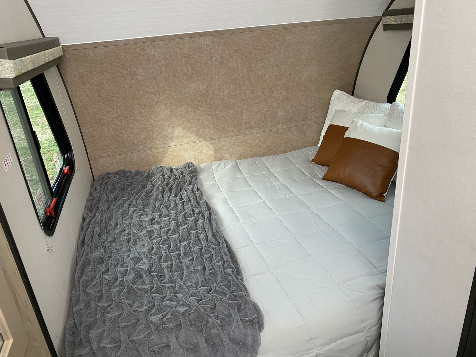 This RV rental's cozy bedroom provides a comfortable sleeping space with a white bed, grey blanket, and accent pillows.. Forest River R-Pod 2019