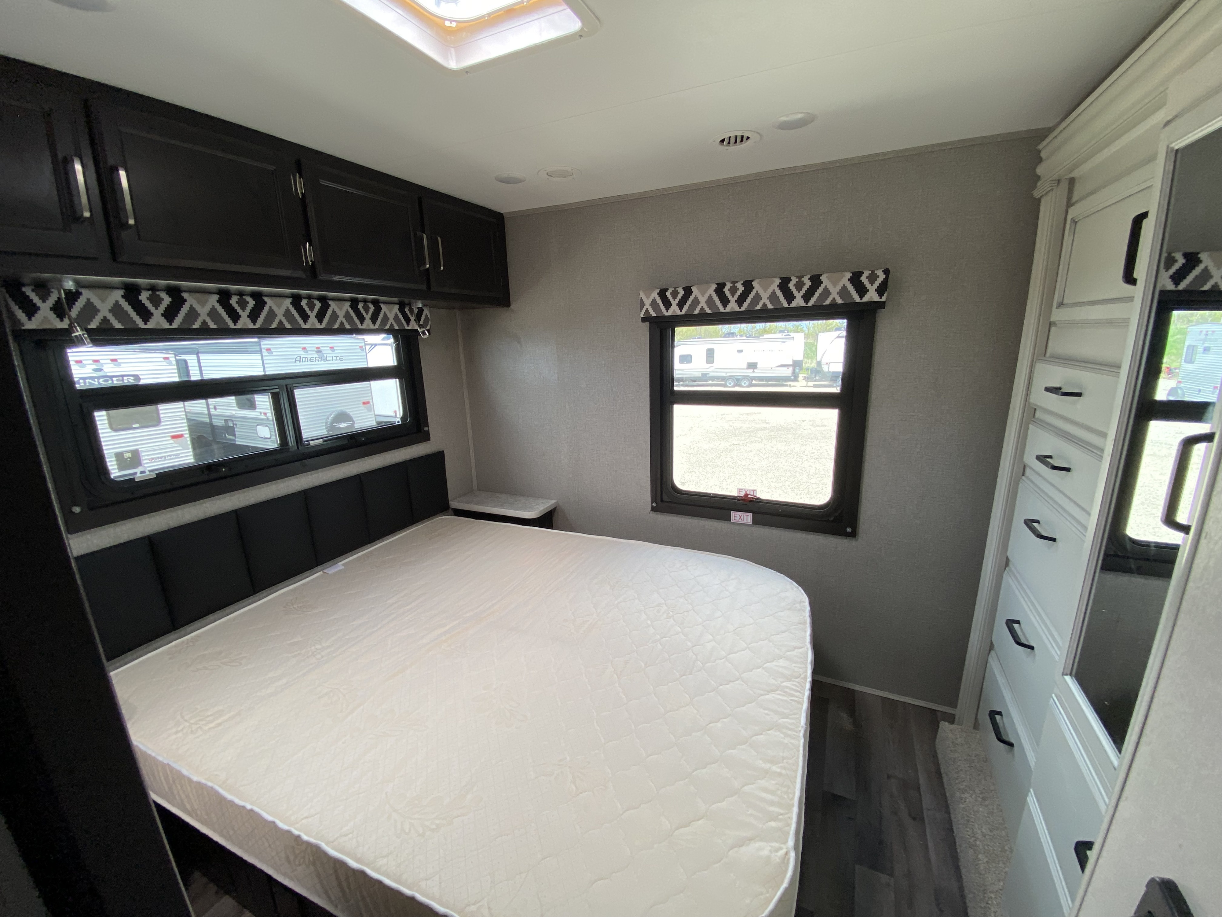 Interior of an RV rental bedroom with a comfortable bed, dark overhead cabinets, and a tall dresser. Ready for your trip!. Jayco Redhawk 2025