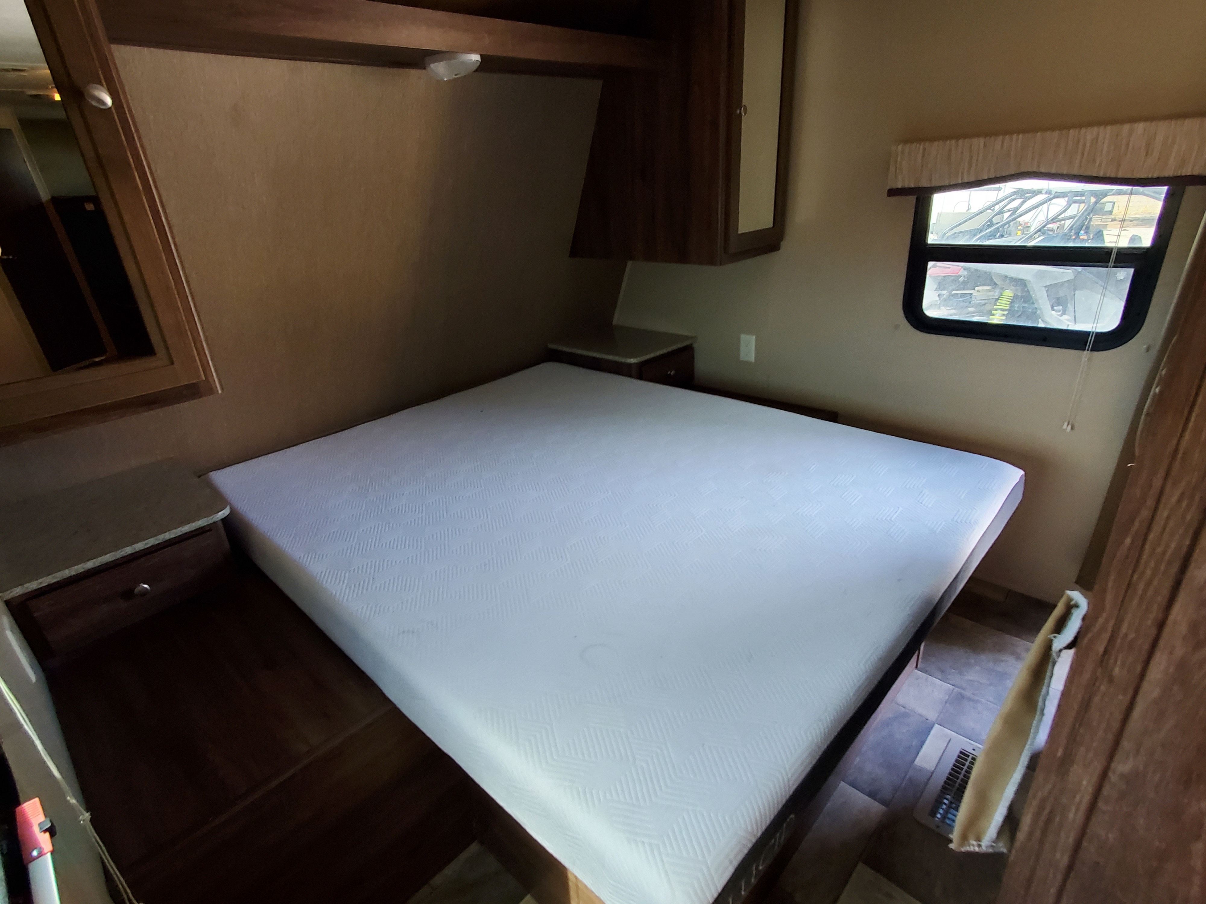 Comfortable RV rental bedroom featuring a pristine white mattress, wooden nightstands, overhead cabinets, and a window view.. Coleman 262bh 2017