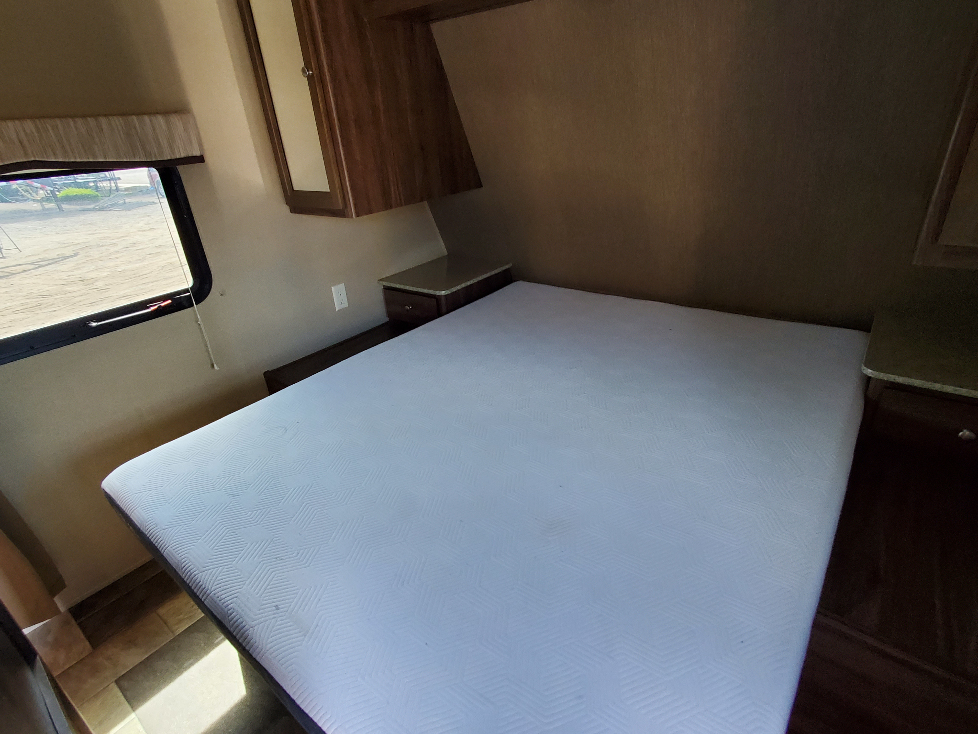 RV rental bedroom interior featuring a large bed, overhead cabinets, and a window with an outdoor view.. Coleman 262bh 2017