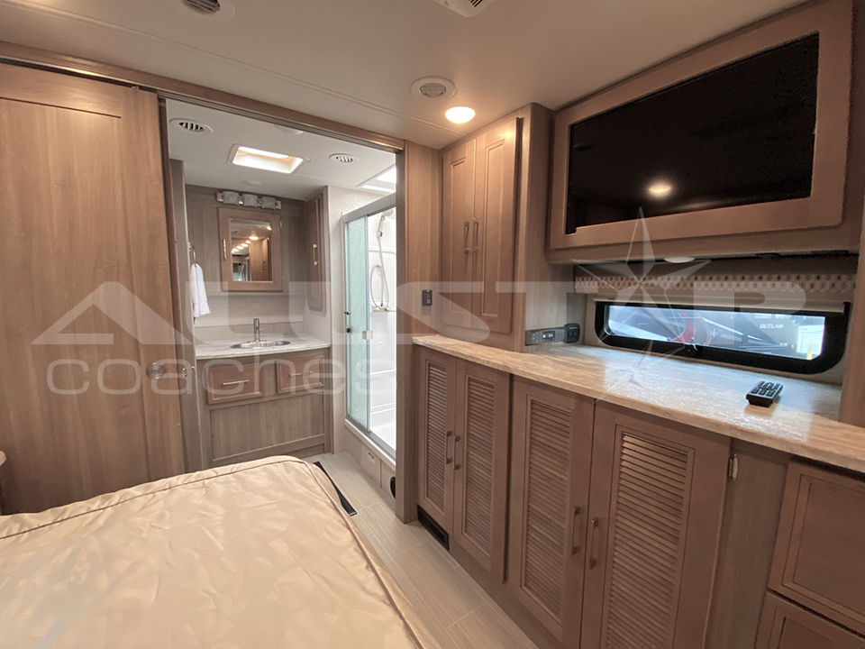 Experience comfort in this RV rental: bedroom with TV, ample storage, and a private bathroom beyond the sliding door.. Coachmen Sportscoach 2020