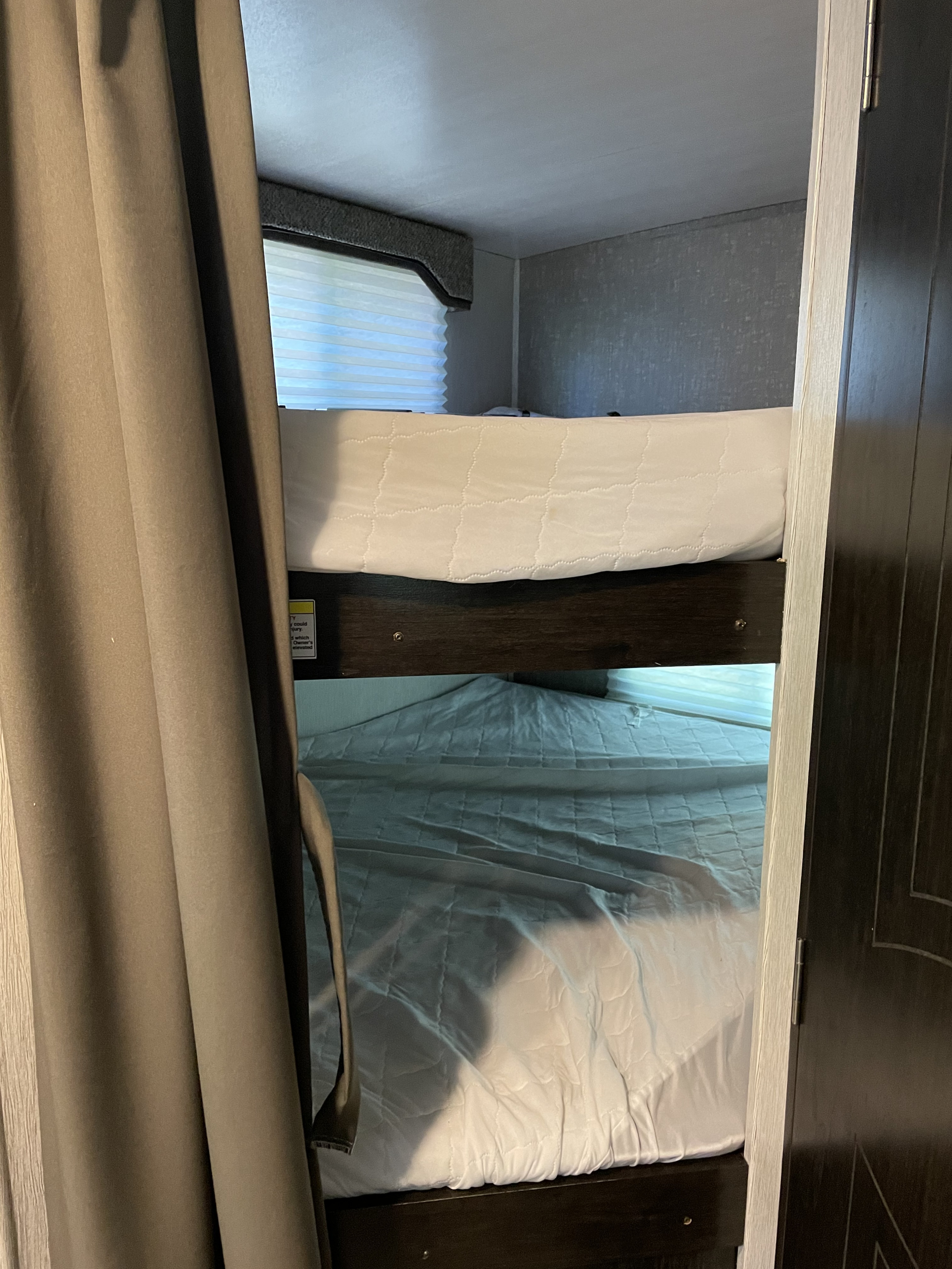 Inside an RV rental: a cozy view of stacked bunk beds with white bedding, perfect for sleeping arrangements on your next adventure.. Heartland North Trail 2019