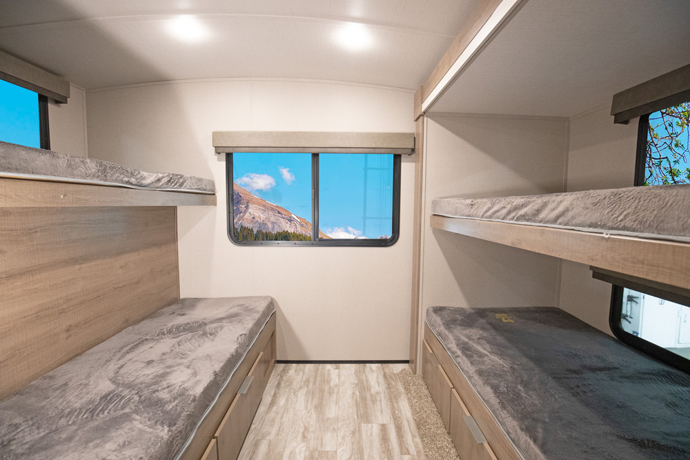 Experience comfort in this RV rental's bunkhouse, featuring cozy gray beds and scenic mountain window views.. Grand Design IMAGINE 3250BH 2021