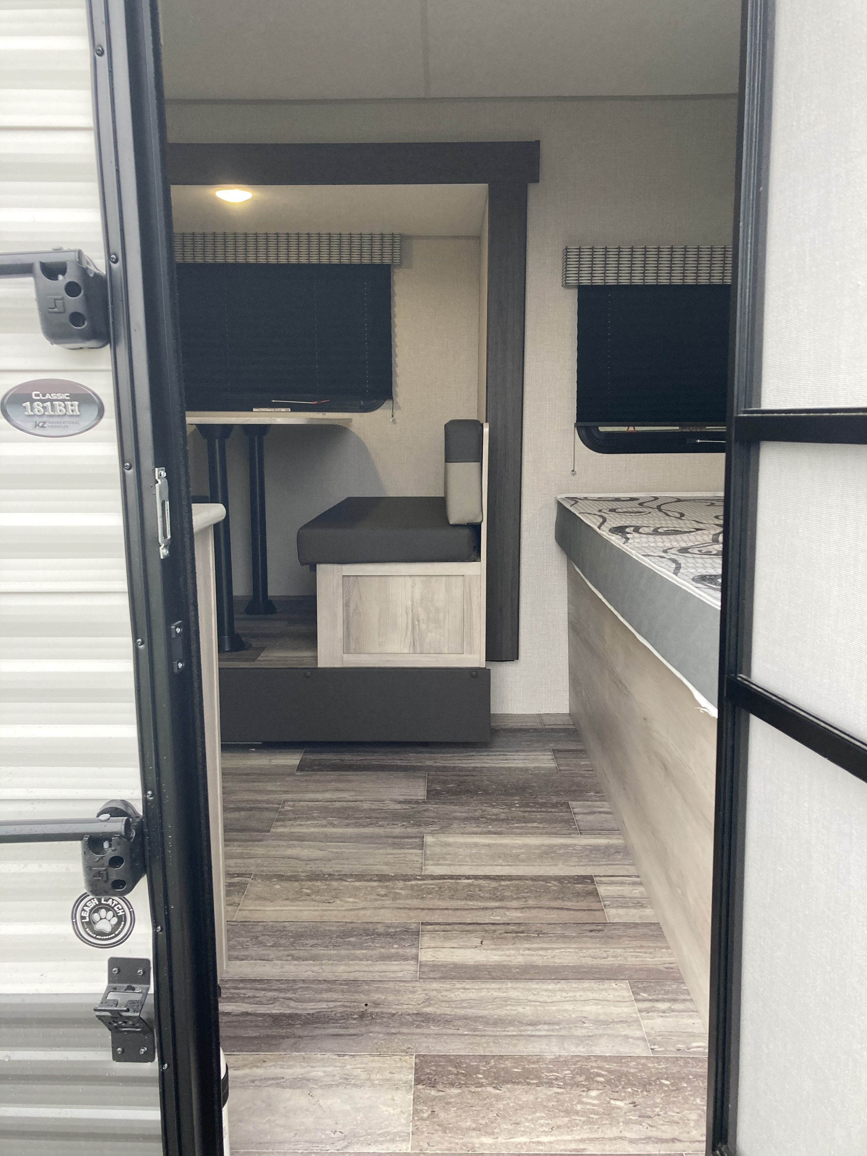 RV rental interior: View into a modern RV with dinette, countertop, and bunk area, featuring wood-look floors.. kz 181bh 2021