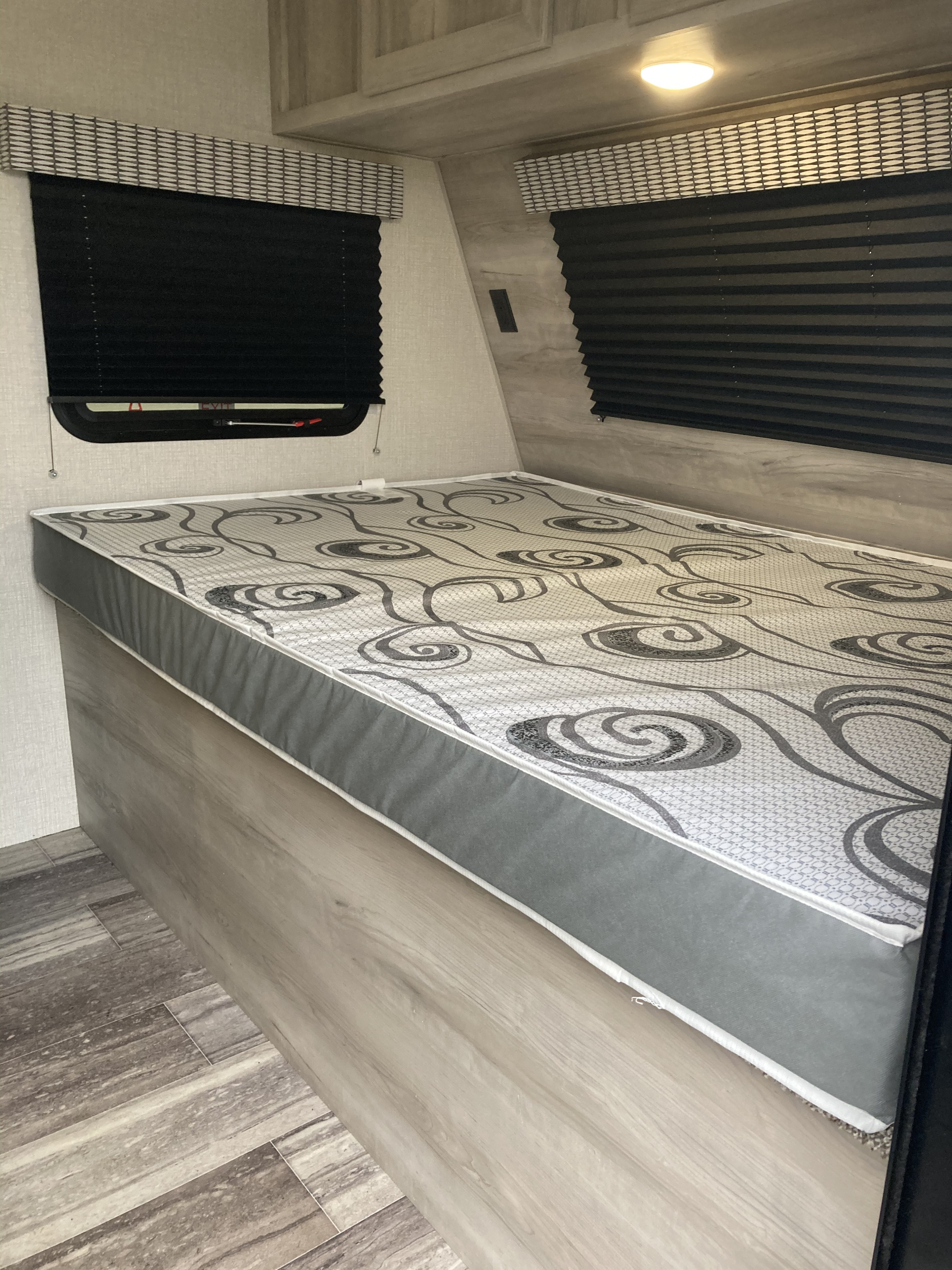 Inside an RV rental unit: a cozy bed with decorative mattress, window blinds, and modern interior finishes.. kz 181bh 2021