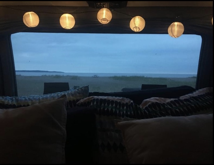 Cozy RV rental interior at dusk: string lights illuminate the bed, with a tranquil beach and ocean view outside.. Roadtrek 190 Popular 1994