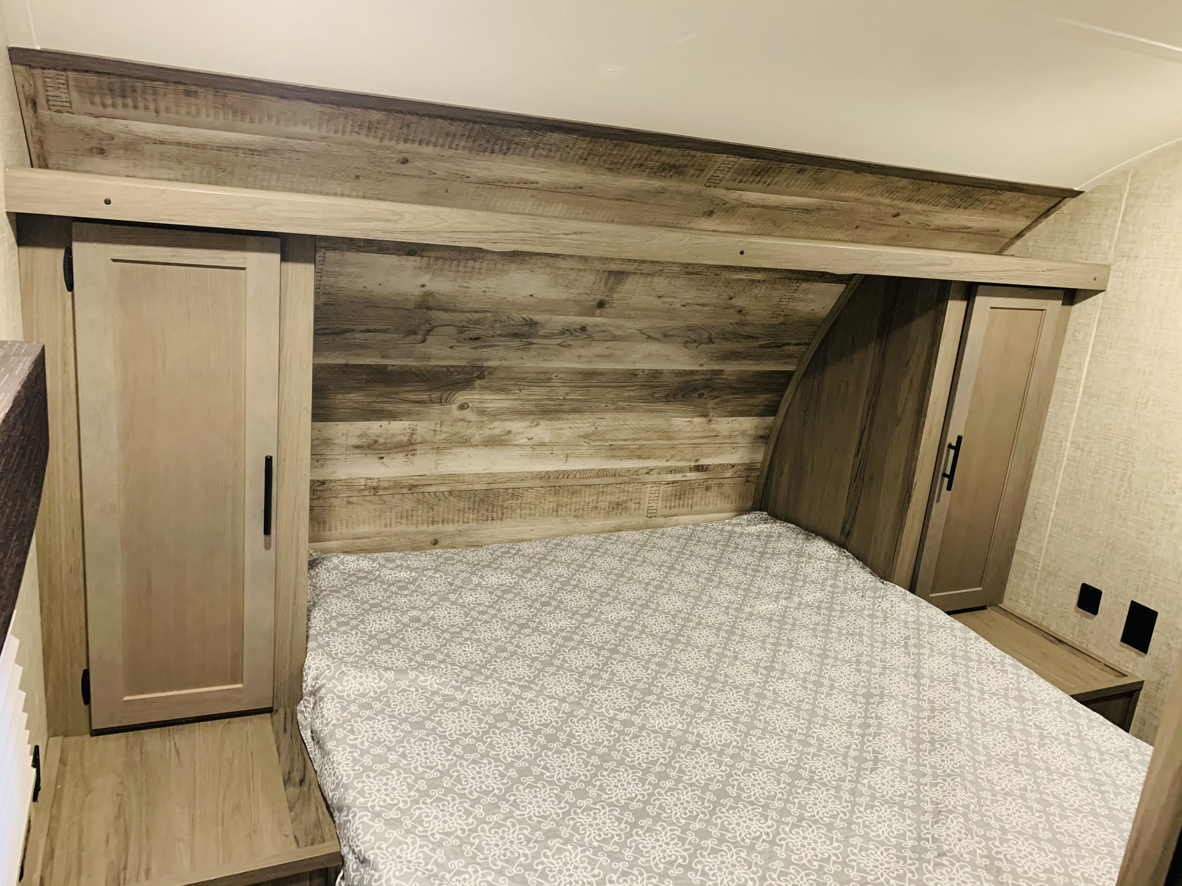 This RV rental's bedroom offers a cozy bed with a patterned sheet, rustic wood headboard, and built-in storage cabinets.. Gulf Stream Gulfstream 2021