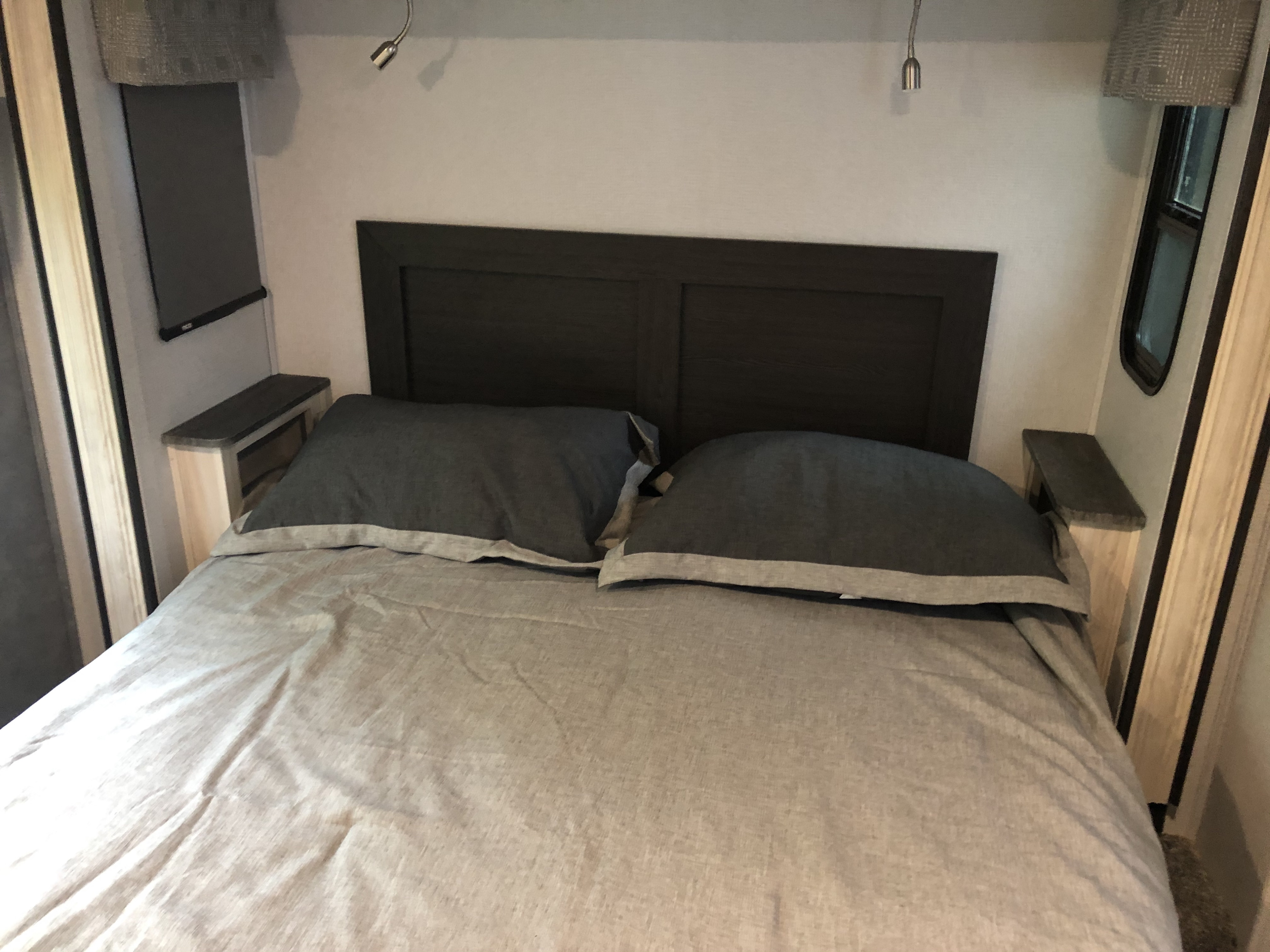 Cozy RV rental bedroom featuring a dark headboard, light gray bedding, and convenient reading lights above a comfortable bed.. Forest River Sunseeker 2021