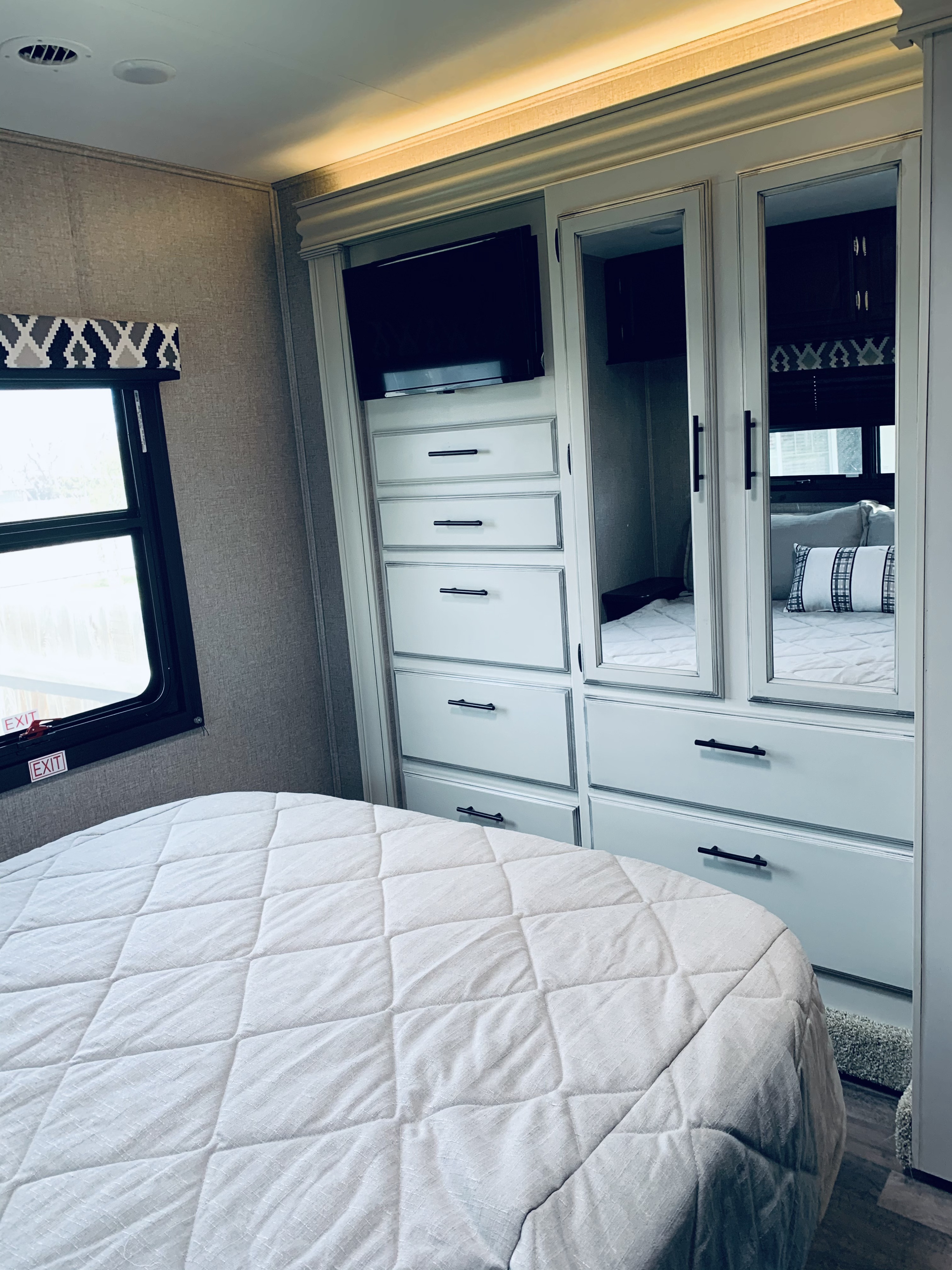 Modern RV rental bedroom featuring a comfy bed, integrated storage unit with TV, and mirrored closet doors. Ideal for travel.. Entegra Coach Odyssey 31F 2021
