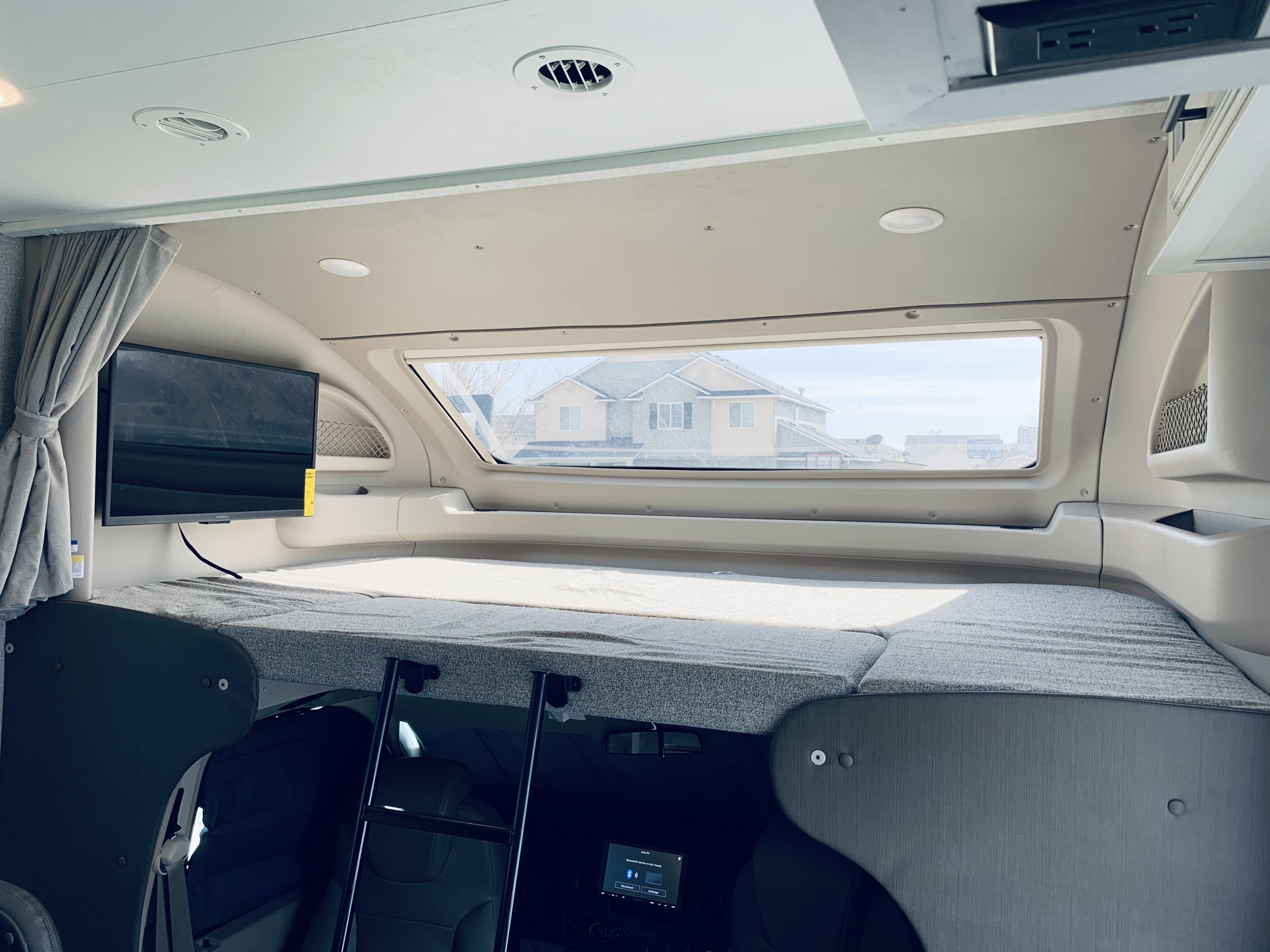 Explore the cozy over-cab bunk sleeping area of this RV rental, featuring a bed, large window, TV, and ladder access.. Entegra Coach Odyssey 31F 2021