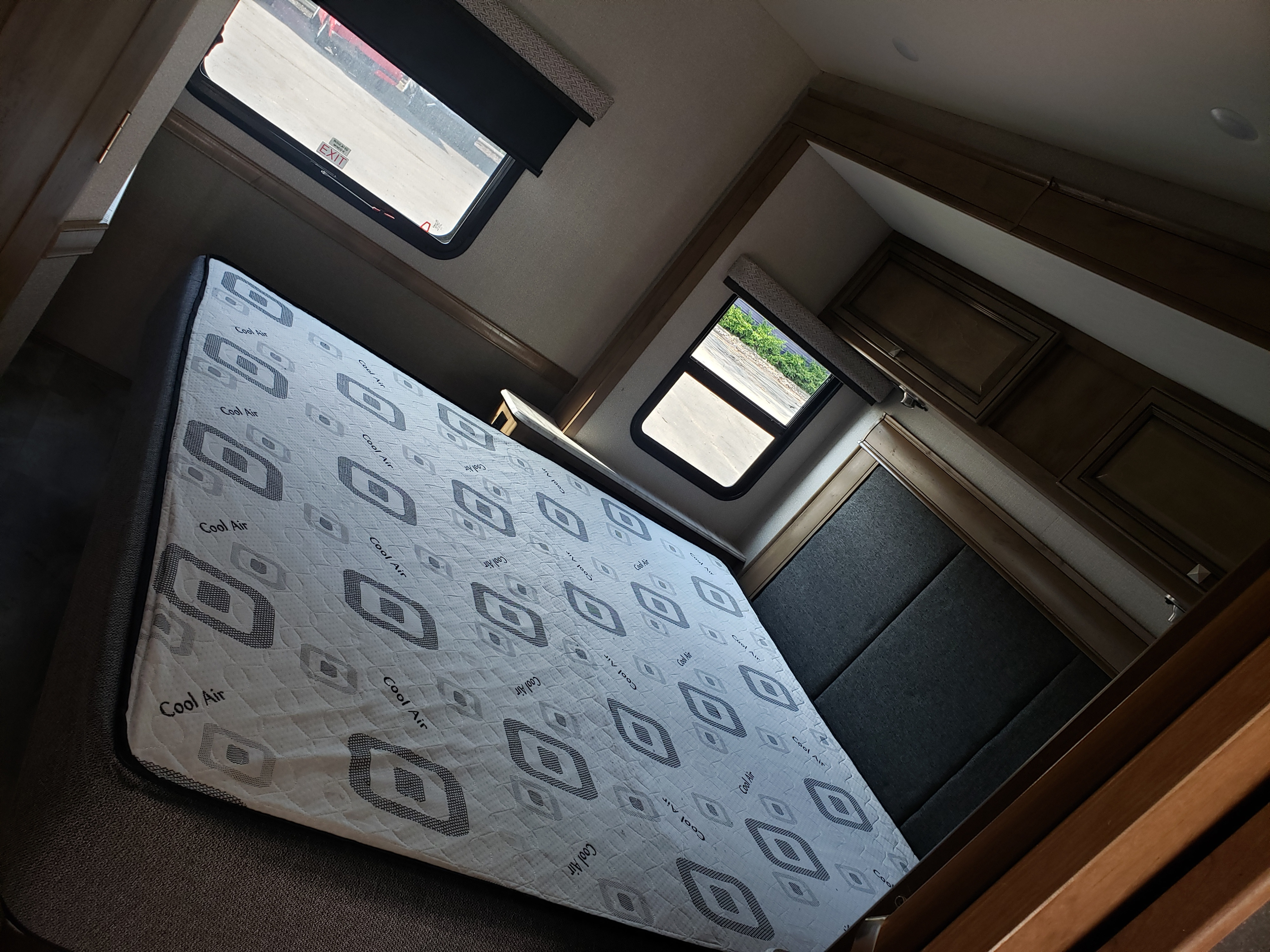 RV rental bedroom features a "Cool Air" mattress, dark headboard, and overhead cabinets. Windows show the exterior view.. Holiday Rambler Admiral 2021