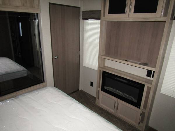 Spacious RV rental bedroom showcasing a bed, mirrored closet, door, and a built-in entertainment center with an electric fireplace.. Coachmen Catalina 2020