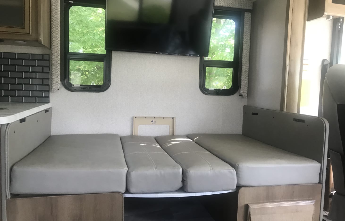 RV rental: Dinette converted to a bed with light gray cushions, dual windows, and a wall-mounted TV for compact comfort.. Holiday Rambler Admiral 2021