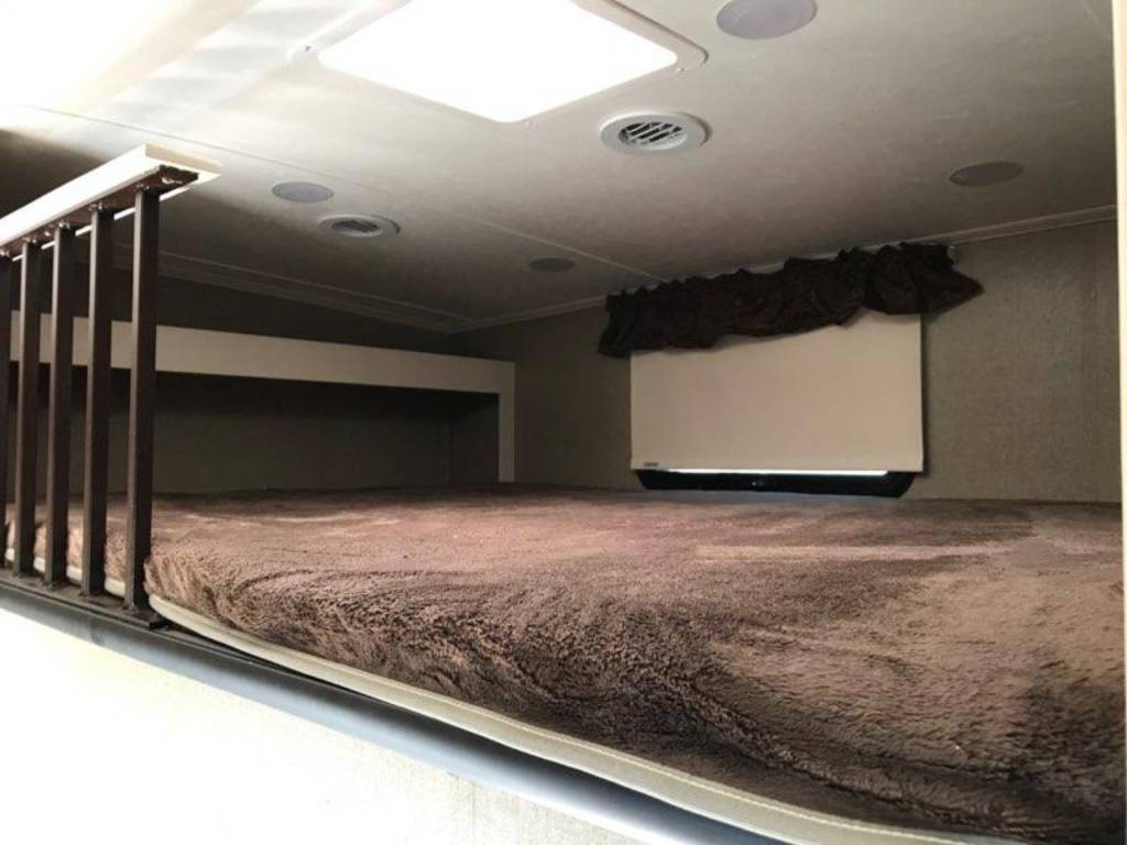 Spacious RV rental bunk bed featuring a plush brown blanket, railing, and window. Ideal for comfortable camper sleeping.. Coachmen Brookstone 2015
