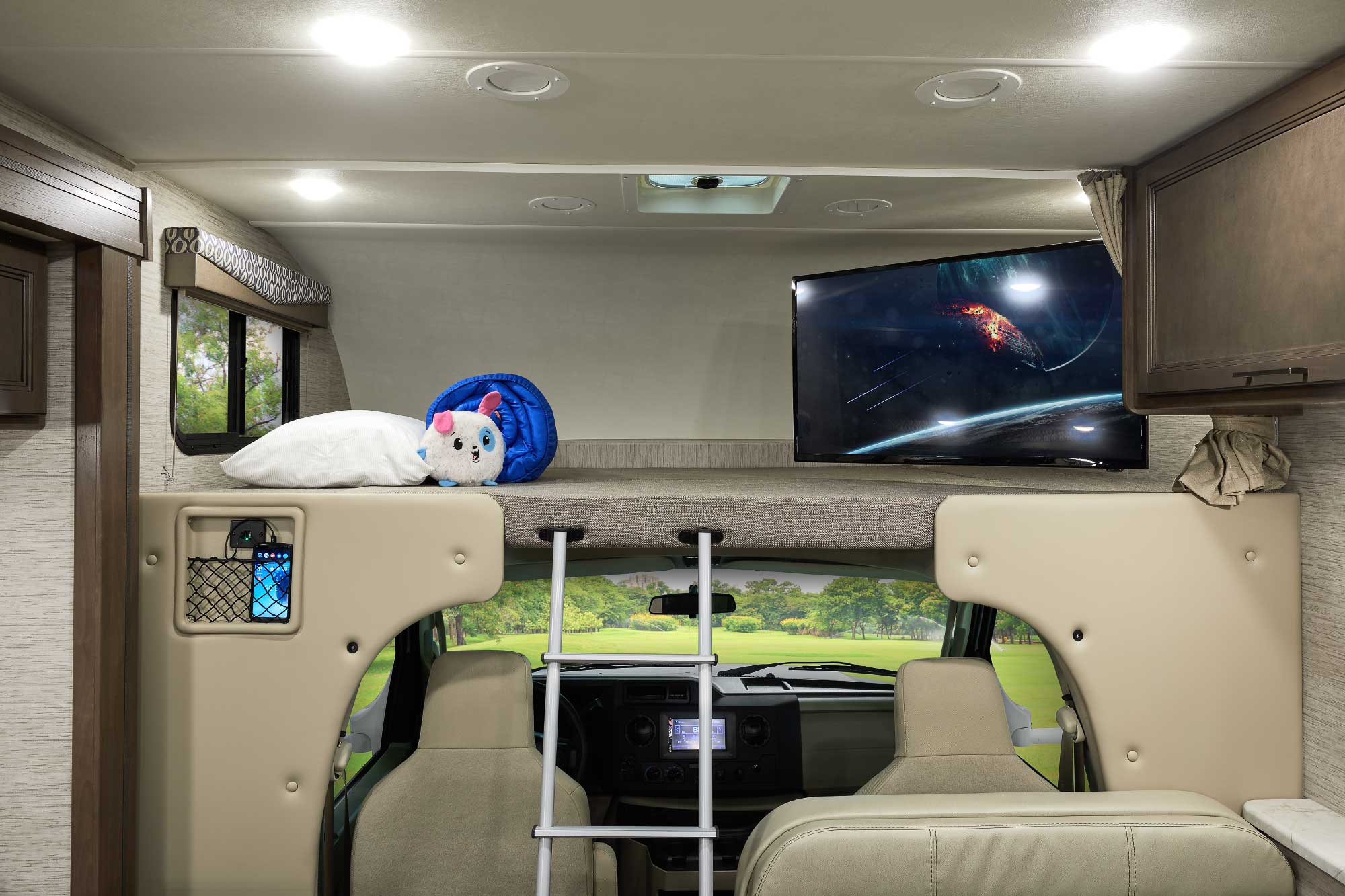 Bright RV rental interior showing a cab-over bunk with TV, pillow, stuffed toy, and ladder over the cabin.. Thor Freedom Elite 2021