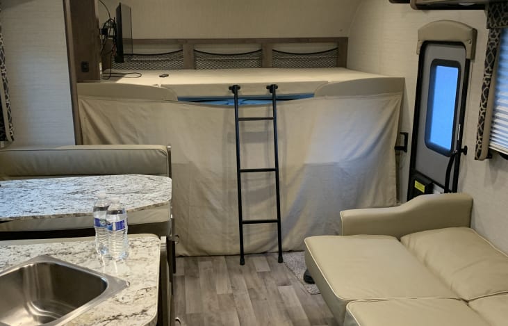 Explore this RV rental interior: bunk beds with ladder, compact kitchen, and living space for comfortable travel.. Jayco Redhawk 2020