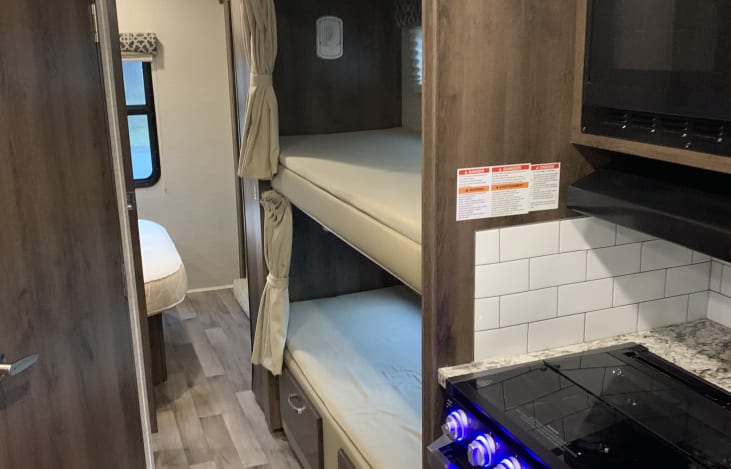 Spacious RV rental interior featuring a modern kitchen, comfortable bunk beds, and private bedroom area. Perfect for travel!. Jayco Redhawk 2020