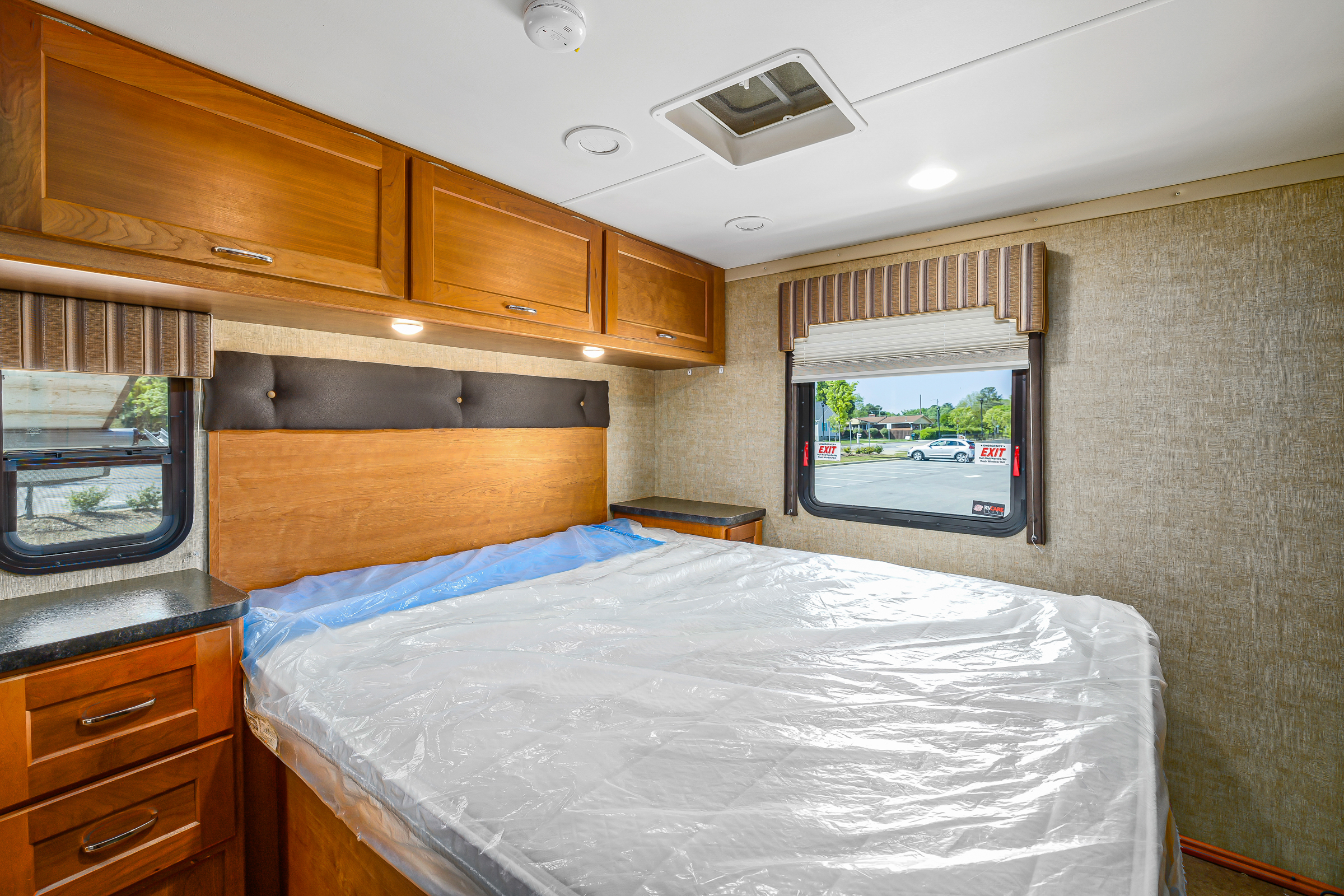 Cozy RV rental bedroom featuring a new bed in plastic, wood cabinets, and windows. Perfect for your next travel adventure.. Winnebago Spirit 2017