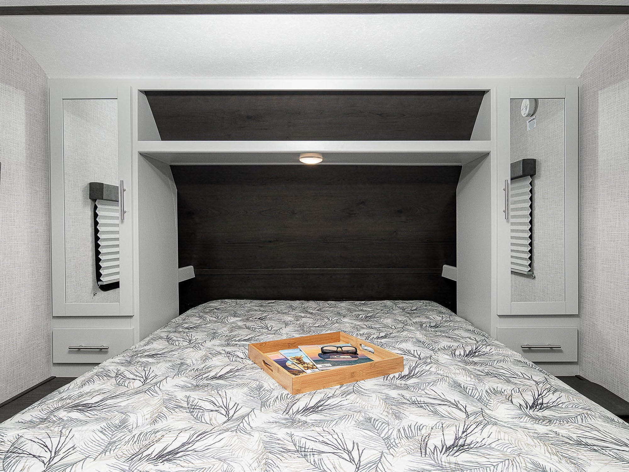 This inviting RV rental bedroom features a neatly made bed with leaf-patterned bedding, built-in mirrored wardrobes, and reading light.. Keystone Bullet 2020