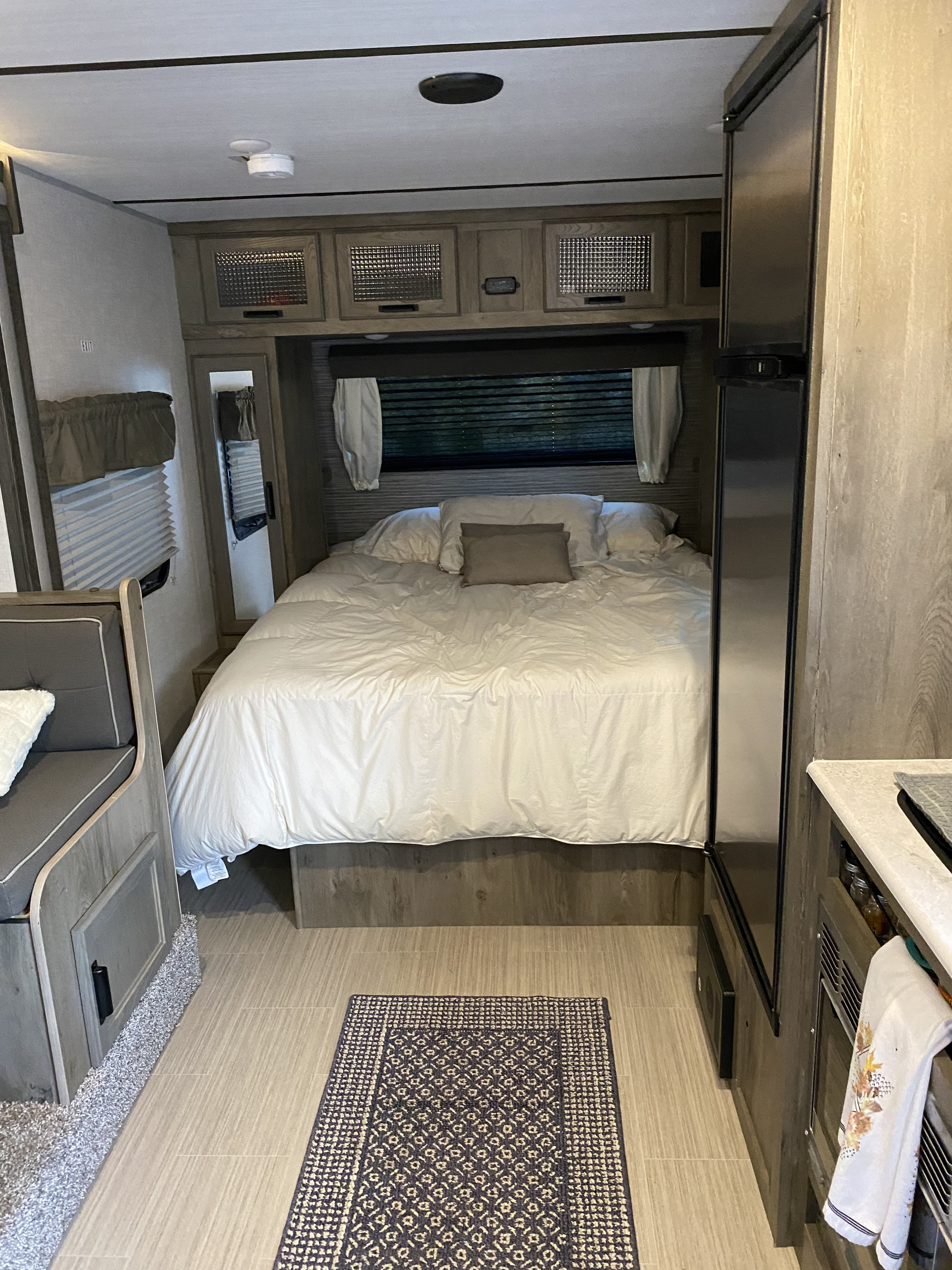 Inside a modern RV rental: a plush queen bed, overhead storage, fridge, and dinette. A cozy home on wheels awaits.. Forest River Surveyor 2021