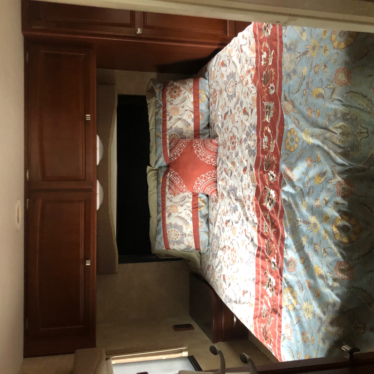 Cozy RV rental bedroom featuring colorful patterned bedding and dark wood cabinets, showcasing a compact yet inviting interior.. Winnebago Chalet 2014