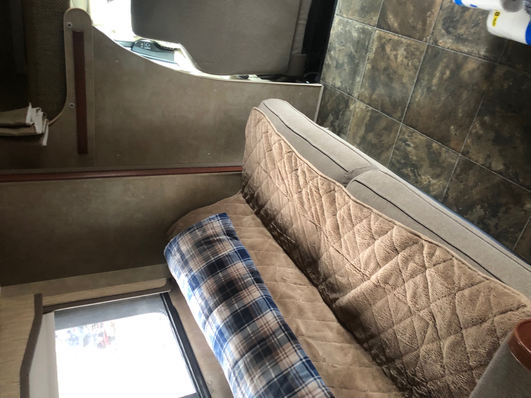 Cozy RV rental interior featuring a soft sofa with a quilted cover, plaid blanket, and practical tiled floor.. Winnebago Chalet 2014