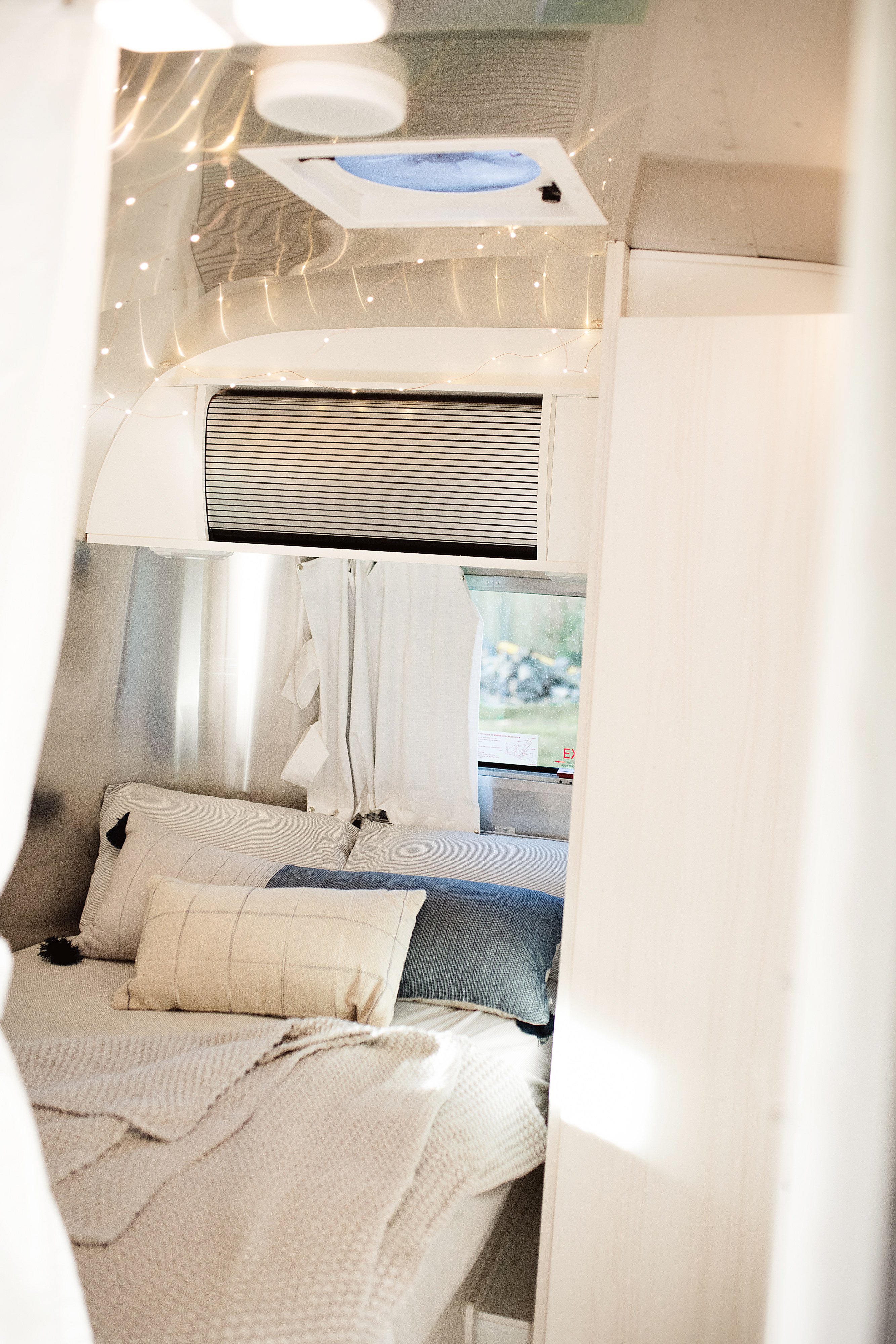 Cozy RV rental bedroom in a travel trailer, featuring fairy lights, soft pillows, and a scenic window view.. Airstream Bambi 2021