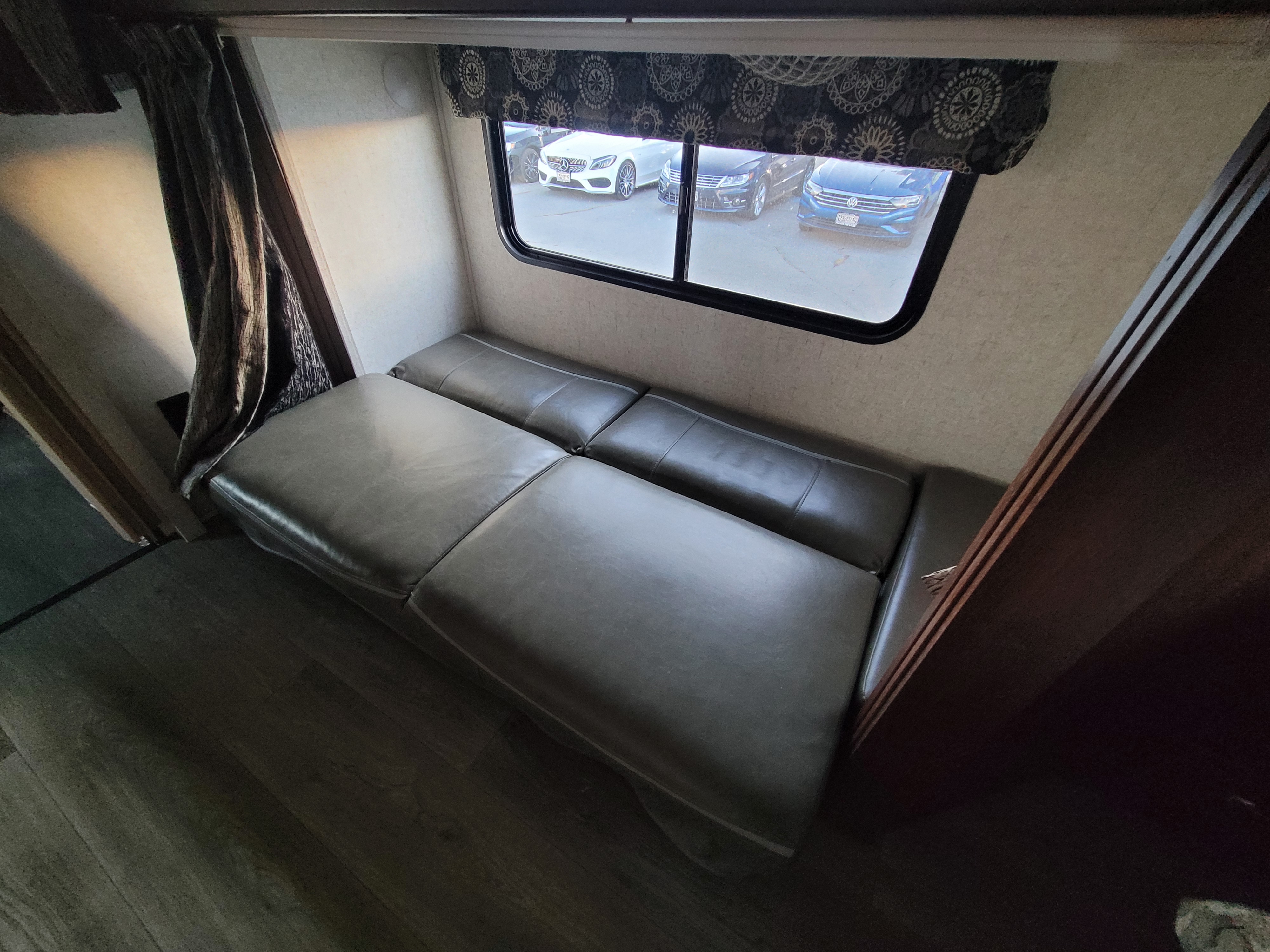 Inside this RV rental: a plush gray sofa-bed next to a large window revealing parked cars.. Forest River Sunseeker 2018