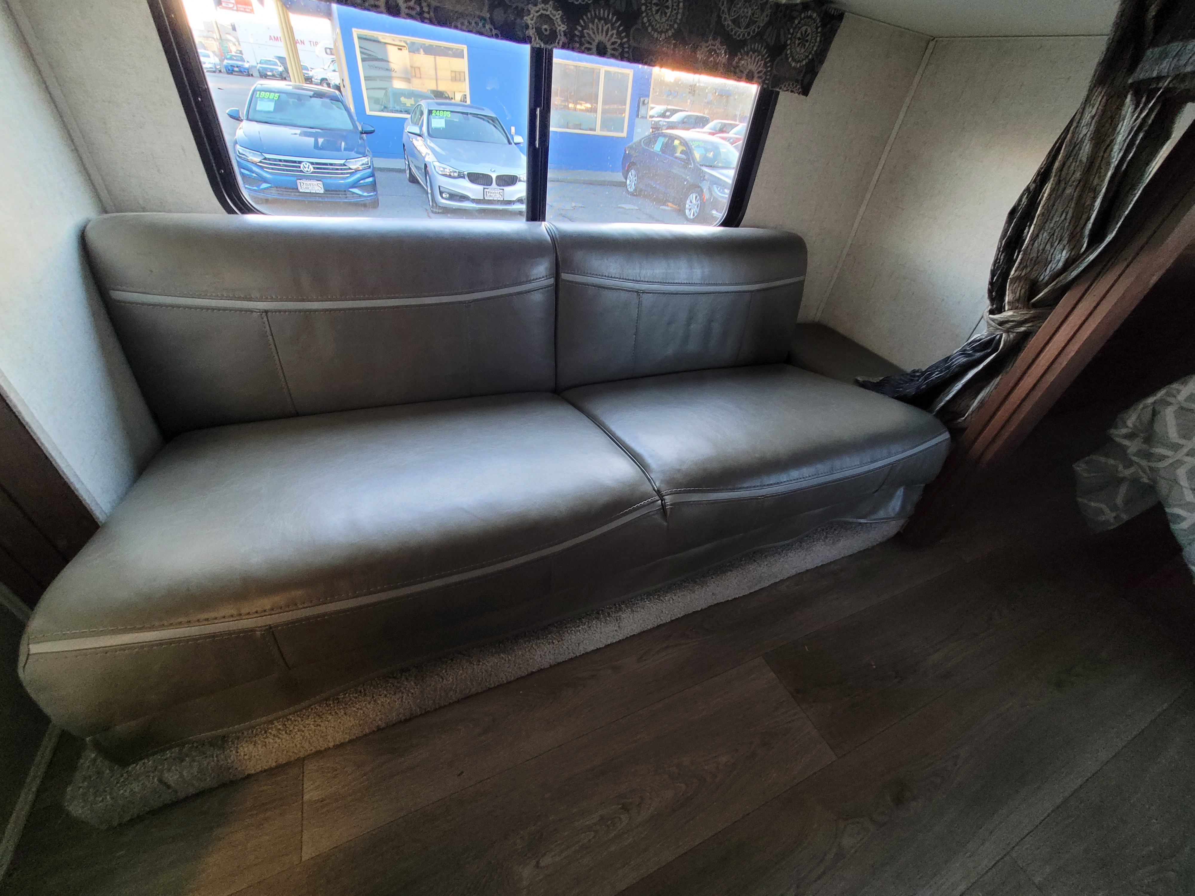 Comfortable sofa inside an RV rental, with a window view of a car dealership, and wood and carpet flooring.. Forest River Sunseeker 2018