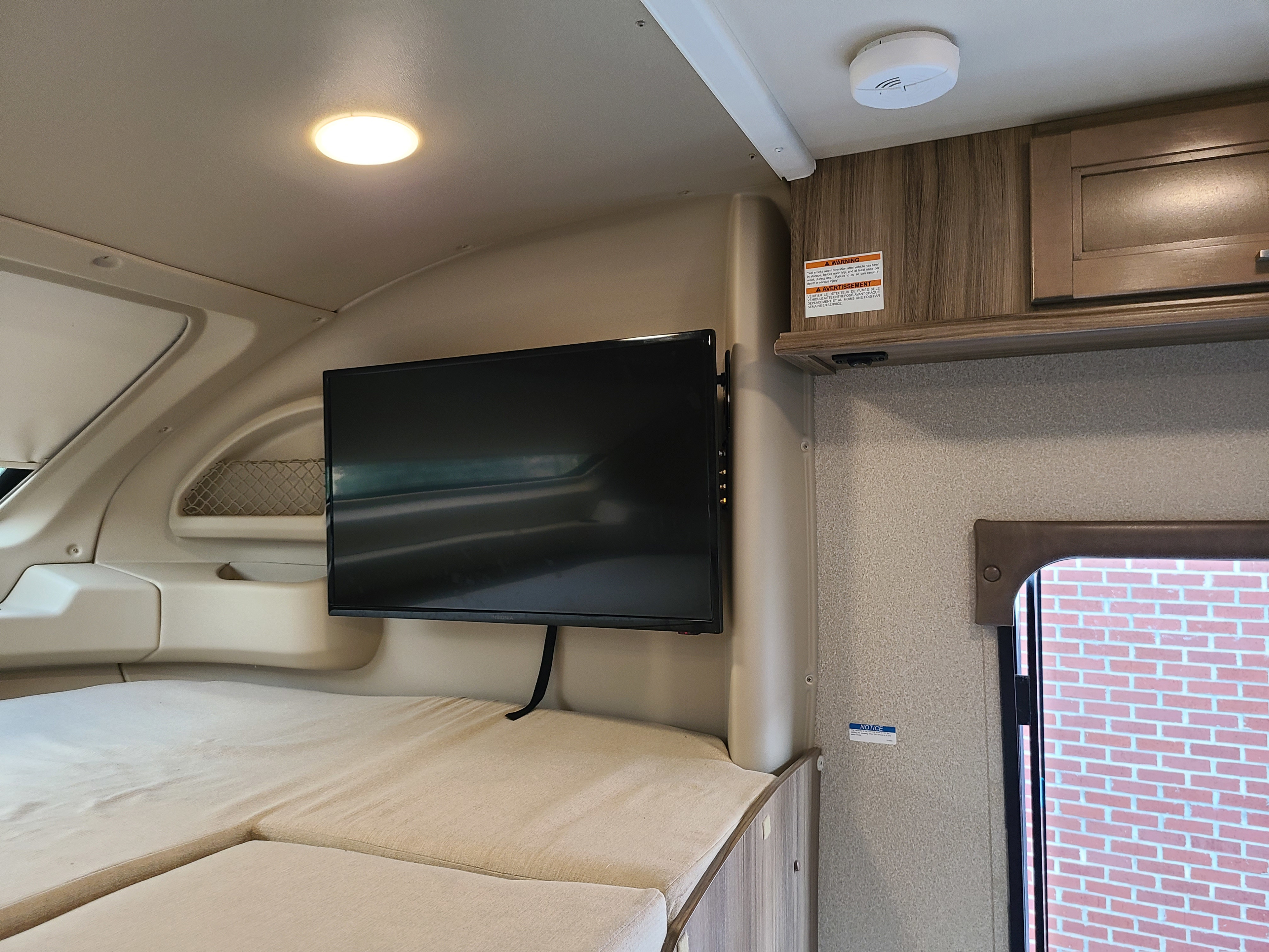 RV rental interior: light sleeping area, wall-mounted TV, overhead light, ceiling smoke detector, and cabinet storage.. Odyssey Entegra 2019