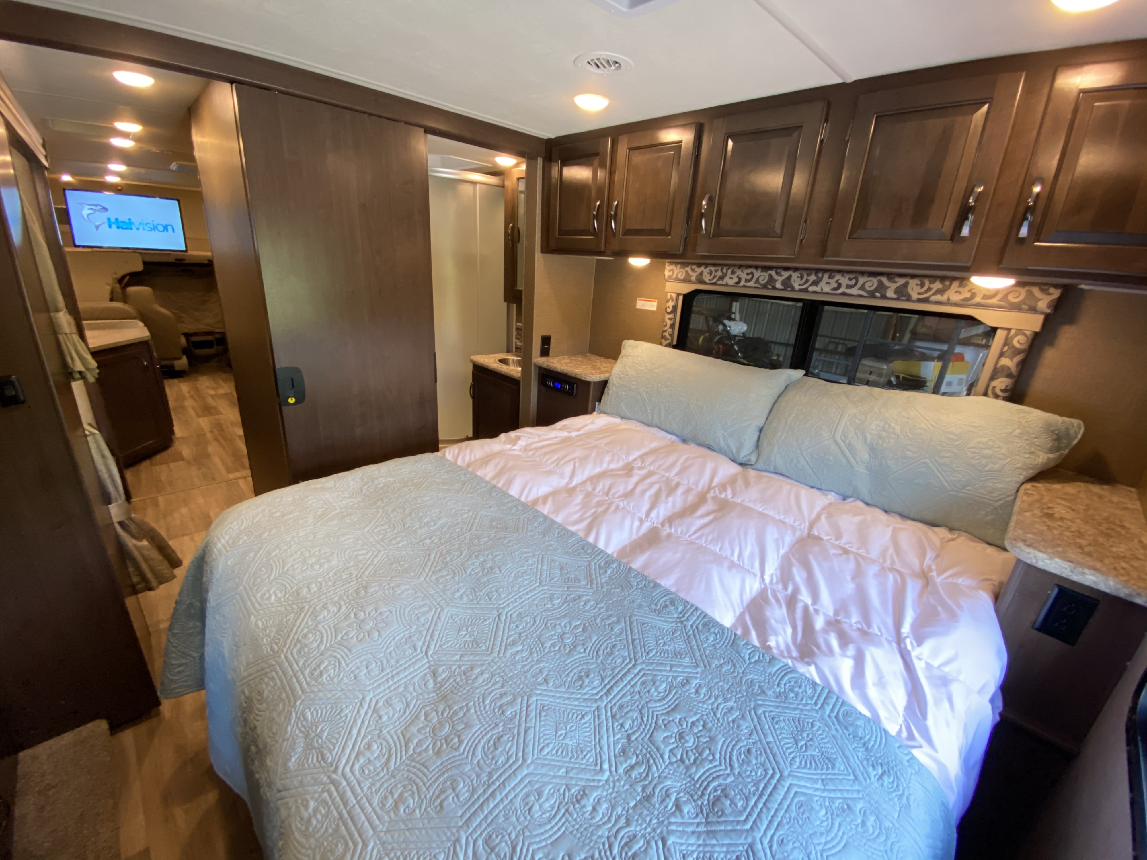 Cozy RV rental interior: main bedroom with quilted bed, built-in cabinets, and a hall to the living area w/ TV.. Thor Motor Coach Four Winds with full wall slide 2018