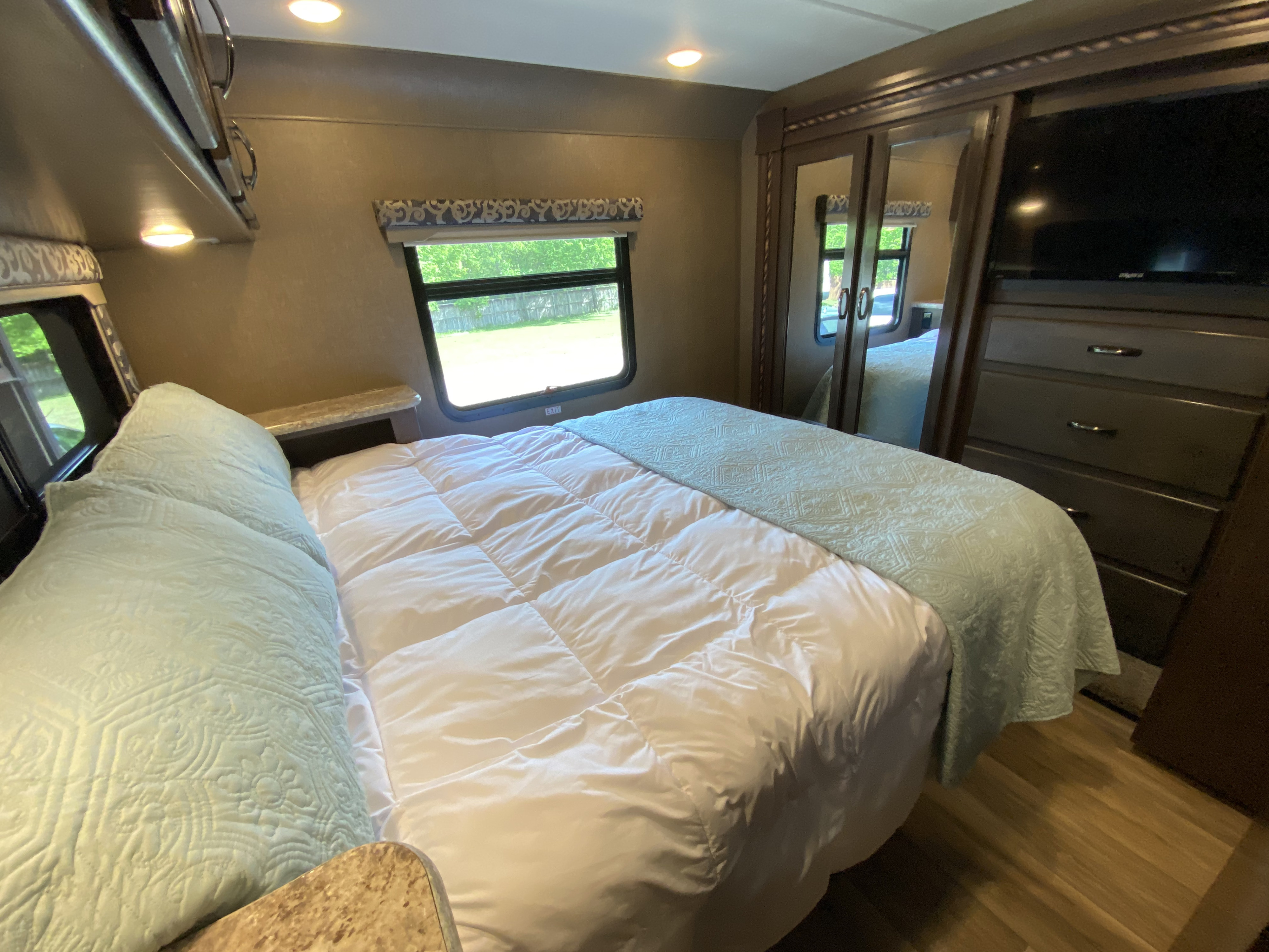 RV rental bedroom: cozy space with bed, storage, TV, window. Light blue & white decor, wood-look floor.. Thor Motor Coach Four Winds with full wall slide 2018