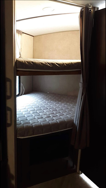 Compact RV rental bunk beds. Two gray quilted mattresses provide sleeping space in this cozy travel trailer bedroom.. Forest River Surveyor 2017