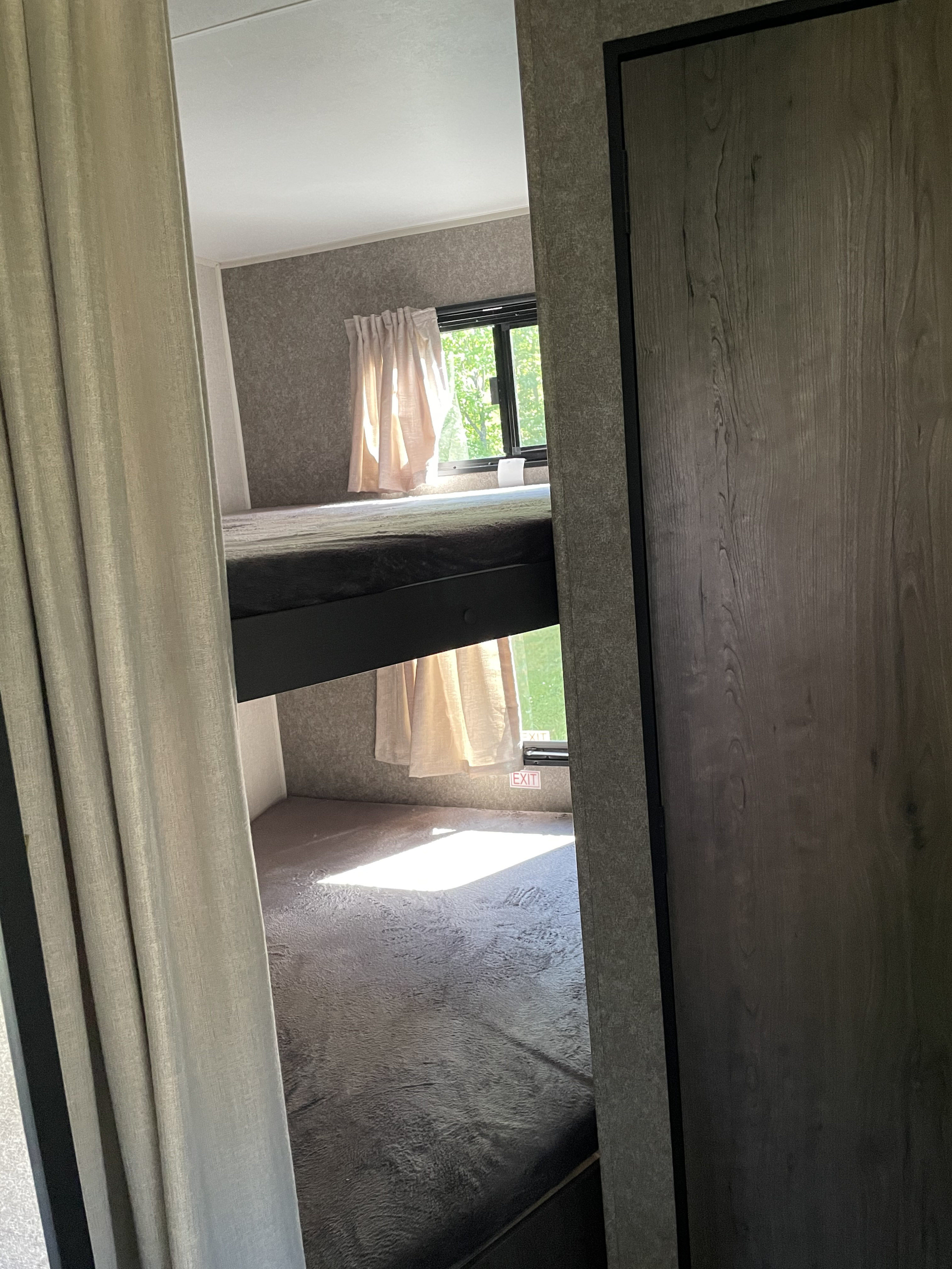 Cozy bunk beds in an RV rental, with a bright window showing green trees, an exit sign, and textured walls.. Starcraft Autumn Ridge 2021