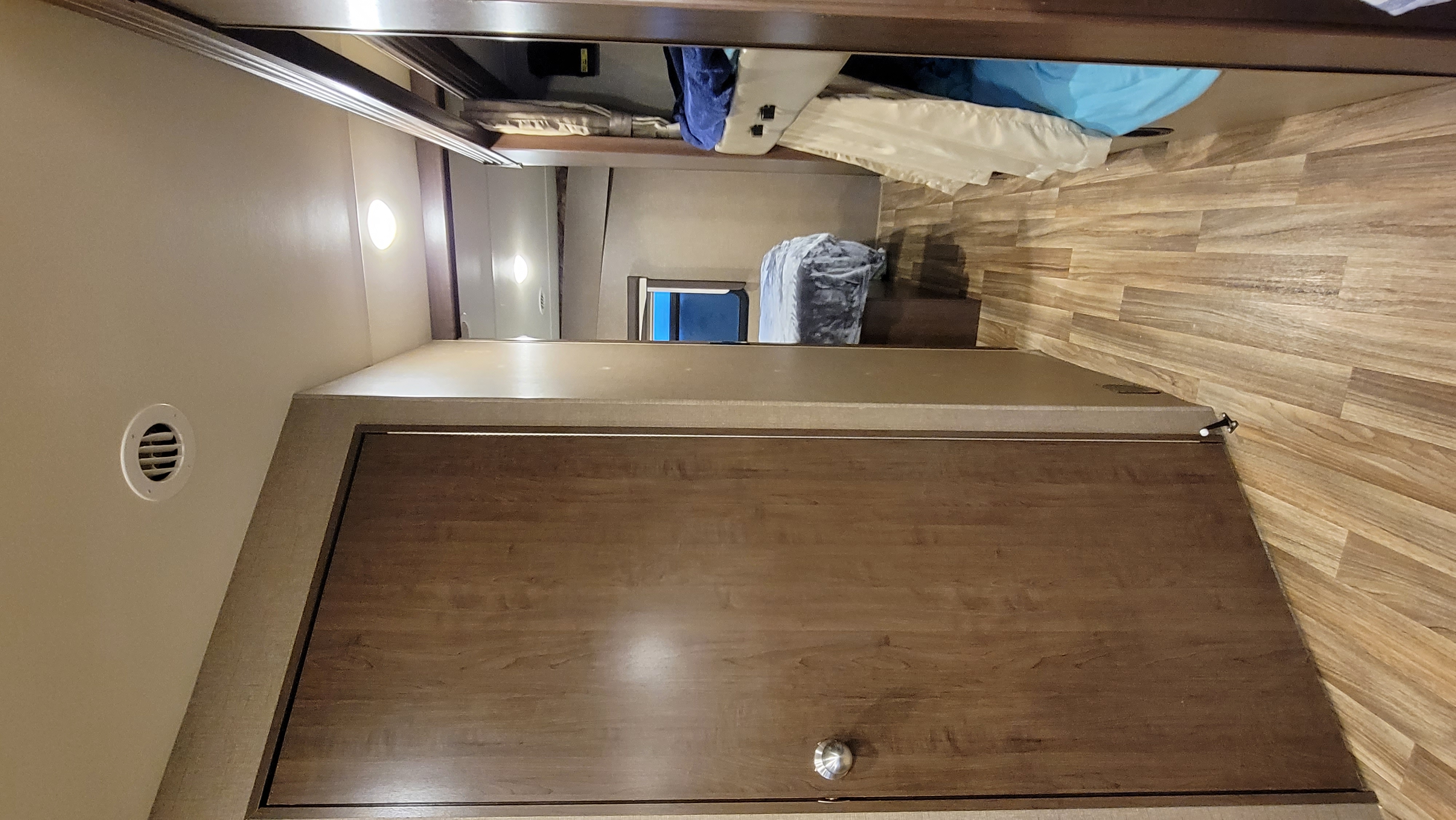 View of an RV rental bedroom showing a bed with blue covers, wood floor, and a closed wooden door in a compact space.. Thor Motor Coach A.C.E 2017