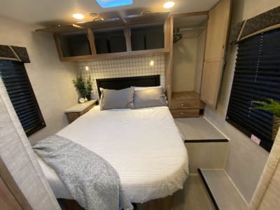 Cozy RV rental bedroom with a queen bed, modern decor, and ample storage cabinets. Ideal for comfortable travel.. Jayco Redhawk 2021
