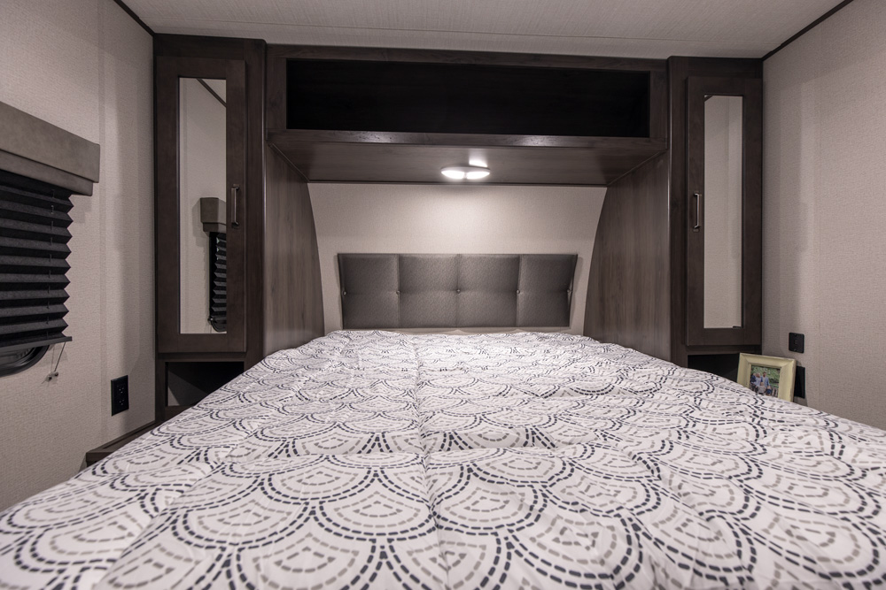 Cozy RV rental bedroom with patterned bed, headboard, overhead storage, and mirrored side cabinets for comfort.. Grand Design Other 2022